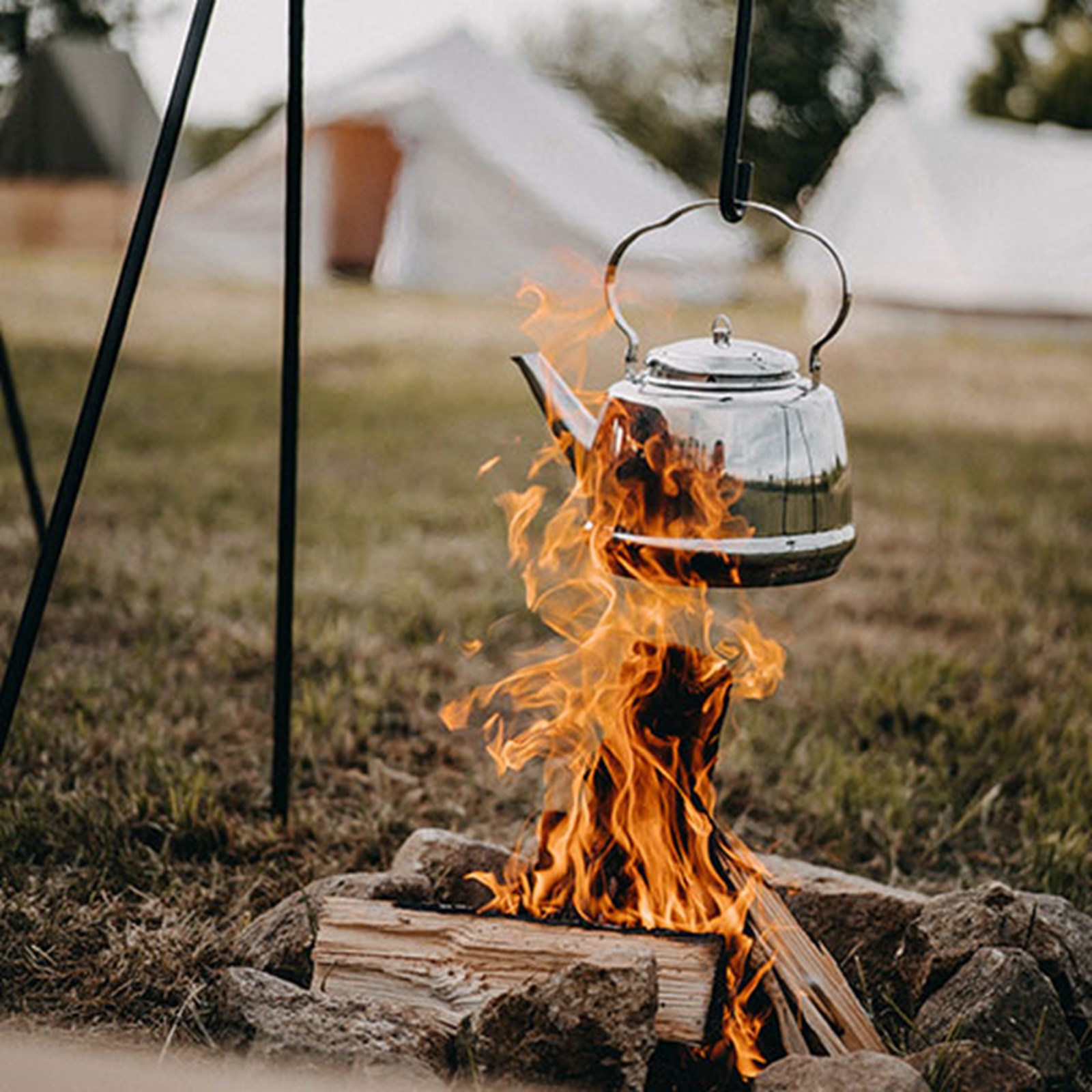 Bålplads med kedel: Madlavning og varme drikke i naturen ved store telte.