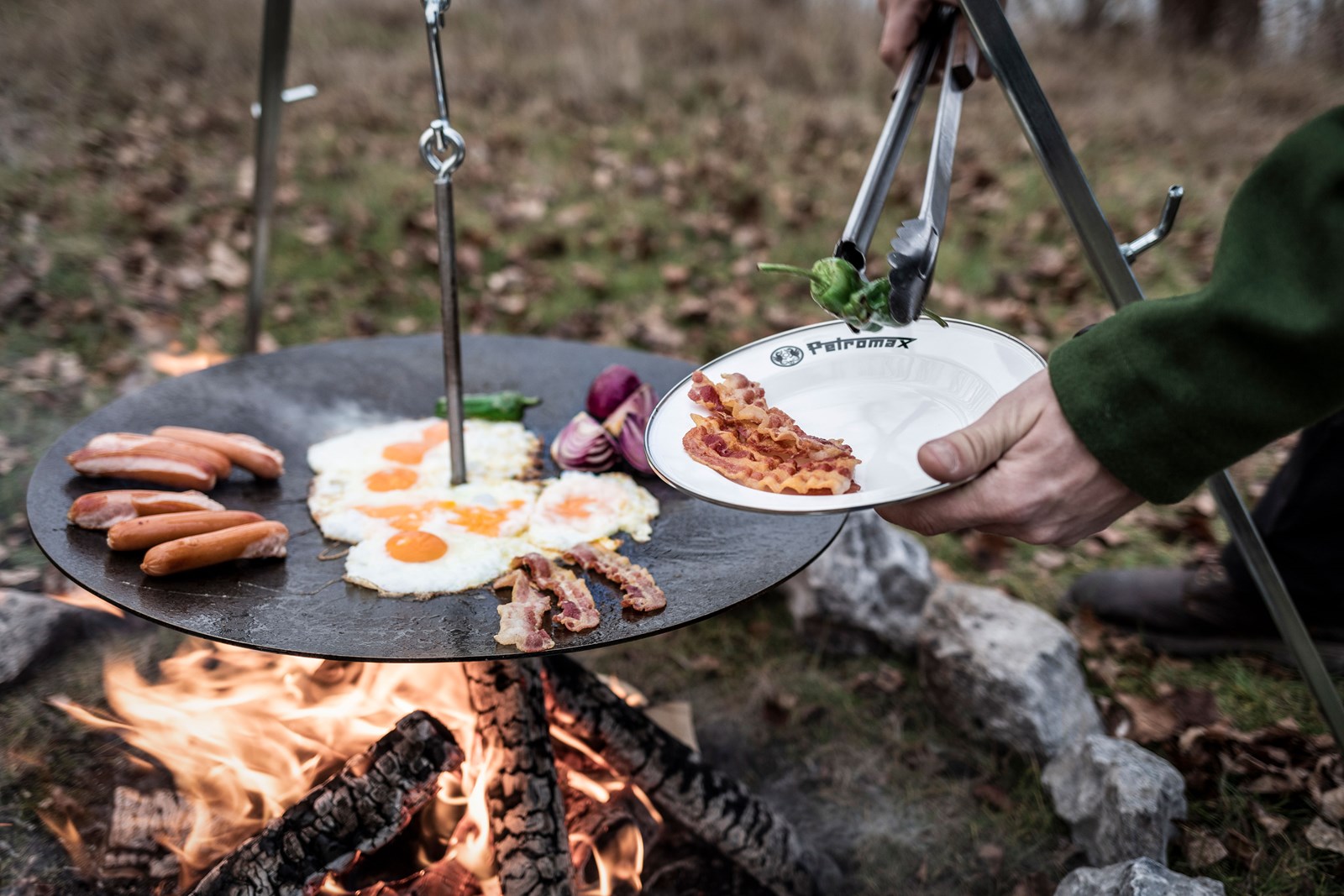 En person laver mad på en stegeplade, der hænger i en Petromax Tripod.