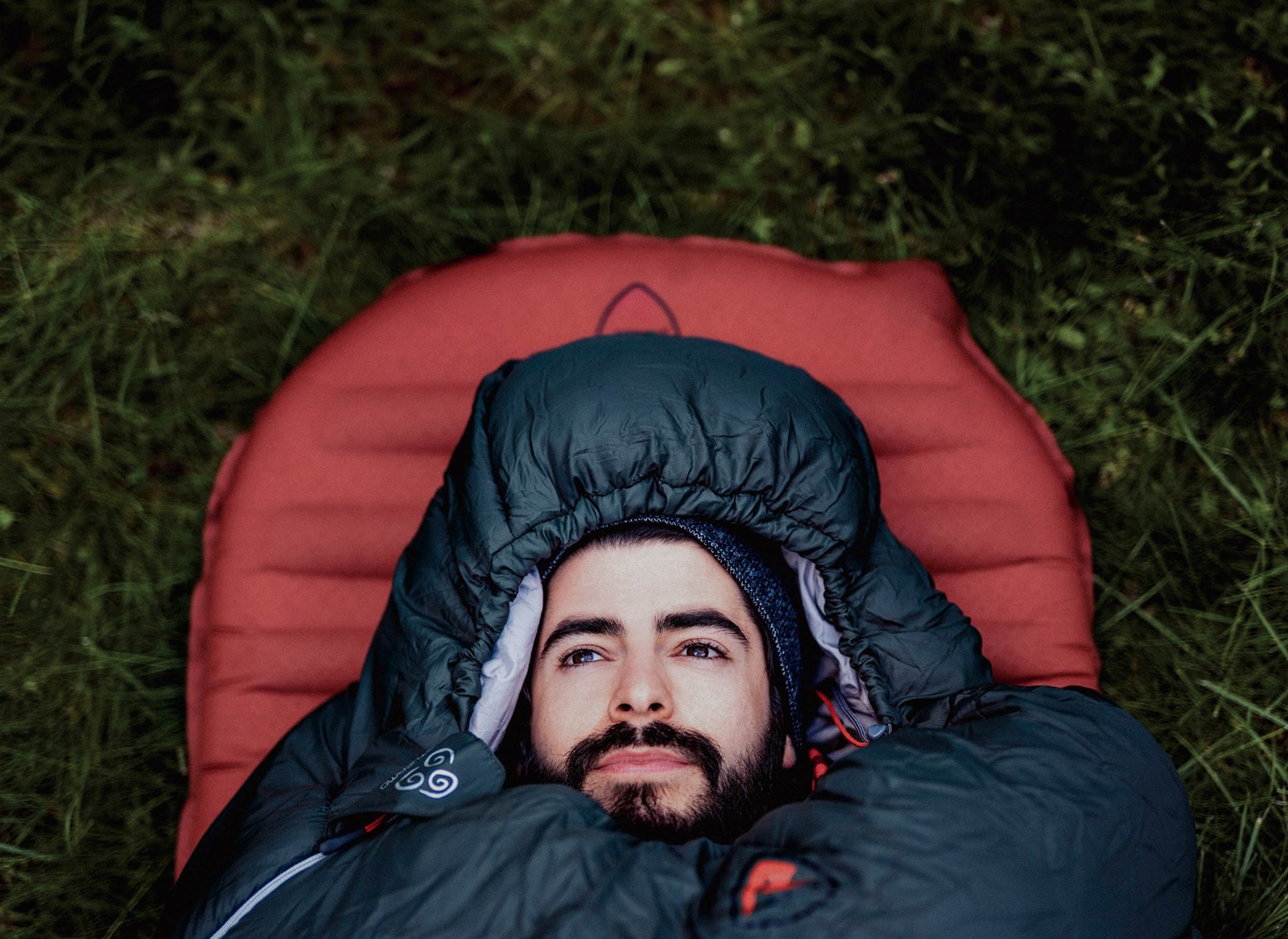 En man der ligger i græsset i sin sovepose.