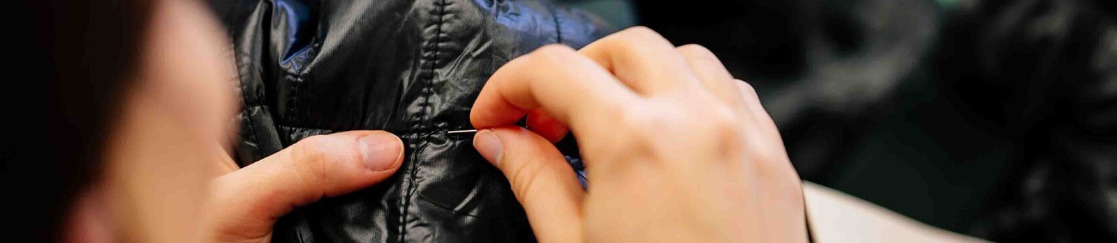 En person der reparere en cotopaxi jakke i hånden.