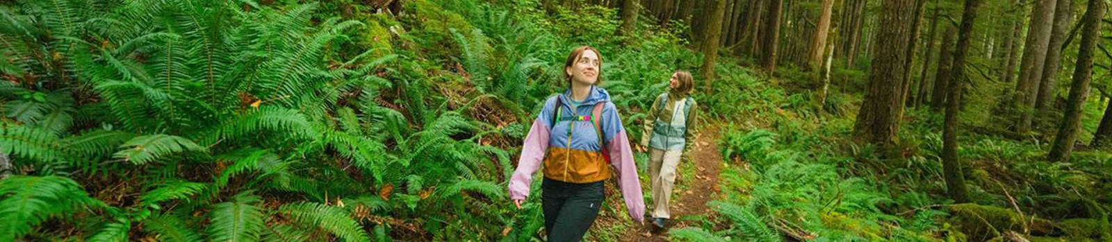 To kvinder der går blandt store bregner iført Cotopaxi.