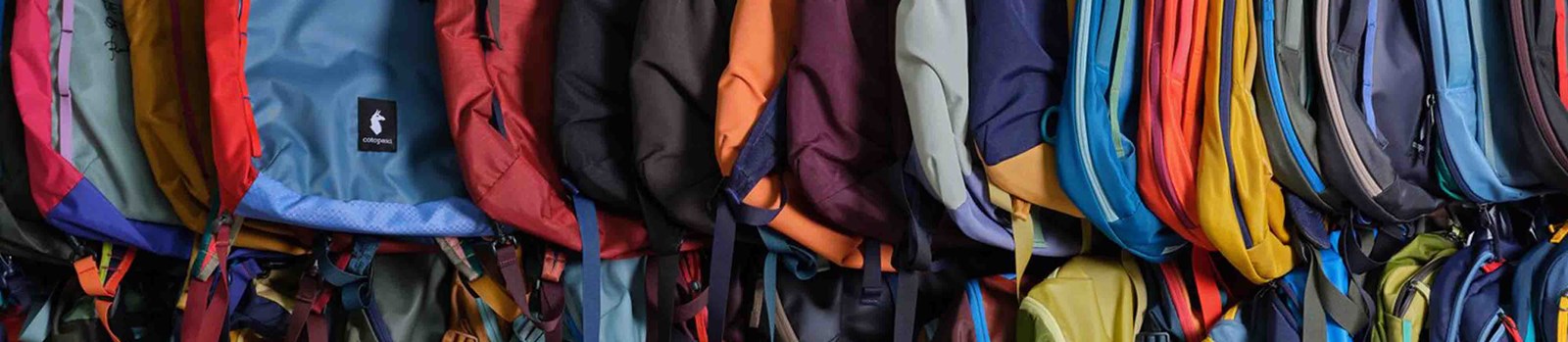 En masse cotopaxi rygsække der hænger i forskellige farver.