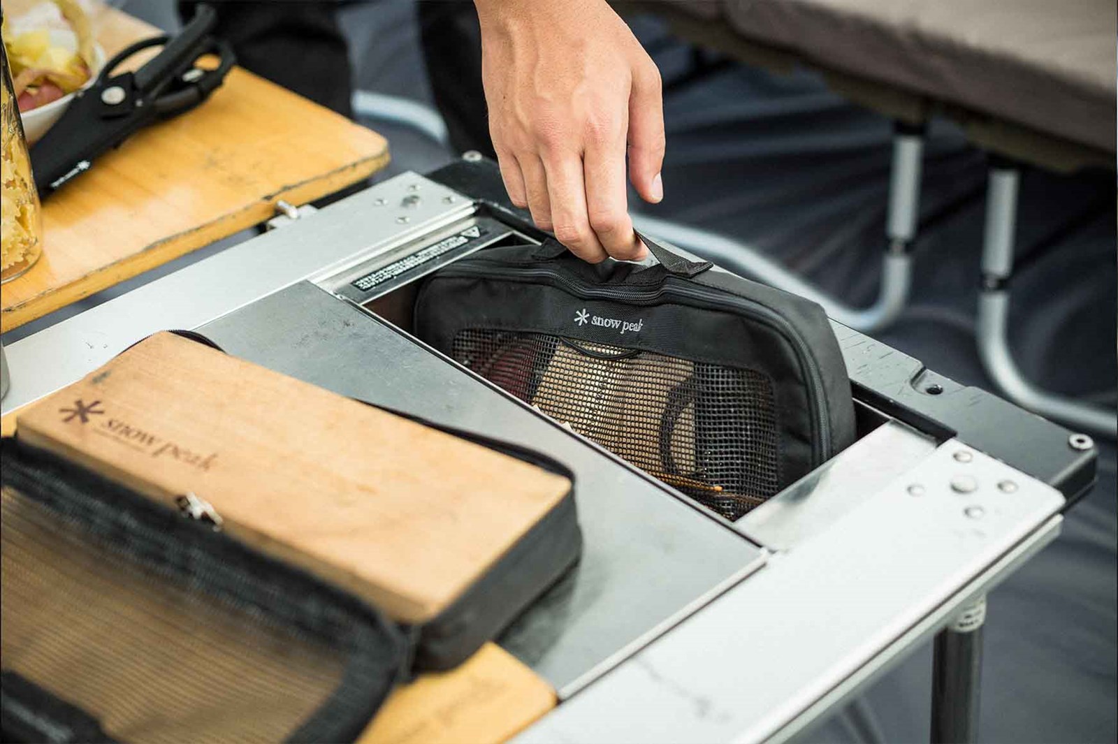 En person løfter noget op af en stålboks der er integreret i et IGT bord fra Snow Peak.