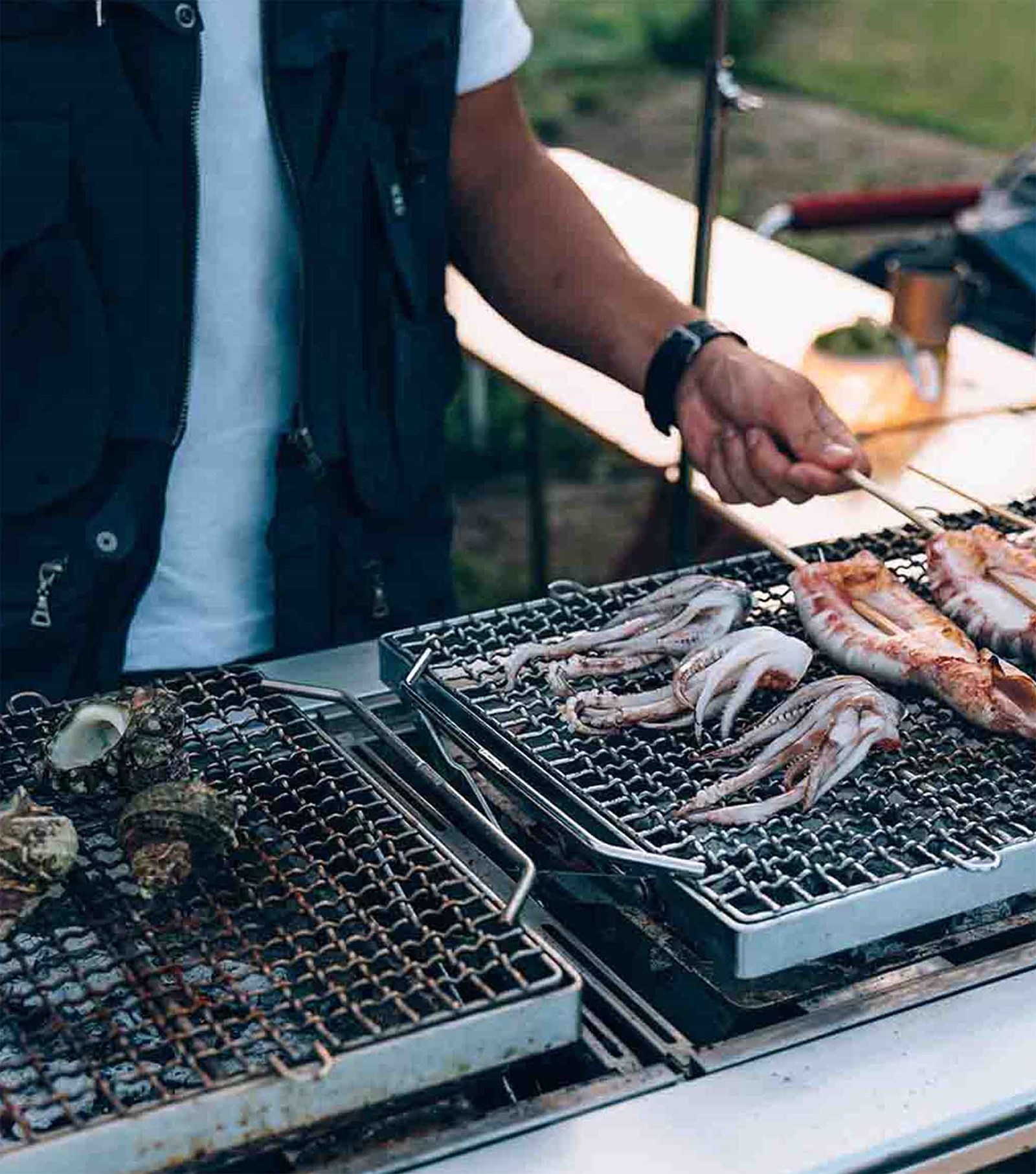 En mand der griller blæksprutter på to BBq boxe der er integreret i IGT Bordet.