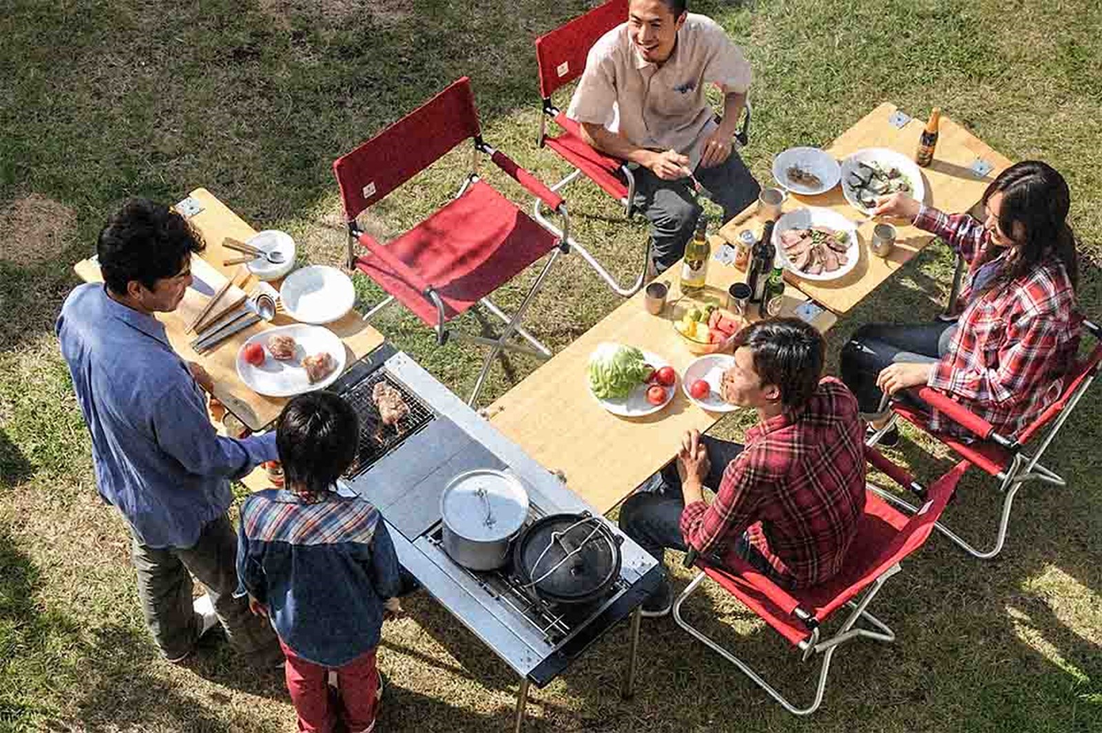 Fem mennesker der nyder et måltid udenfor ved Snow Peaks IGT bord der både har spiseområde og madlavnings station..