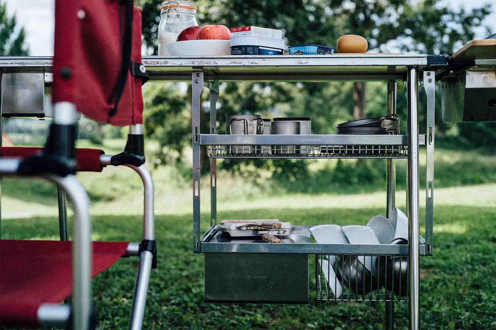 Et udendørs IGT bord med to hylder under med kurve der er fyldt med skåle og kopper.