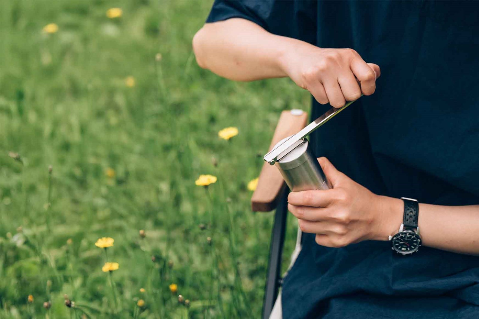 En kvinde der sidder udenfor og maler hendes kaffebønner i en Snow Peak Field Coffee Grinder.