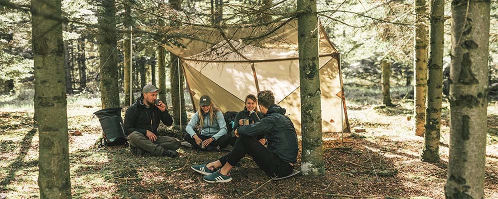 Folk der hygger sig under en tarp i skoven.