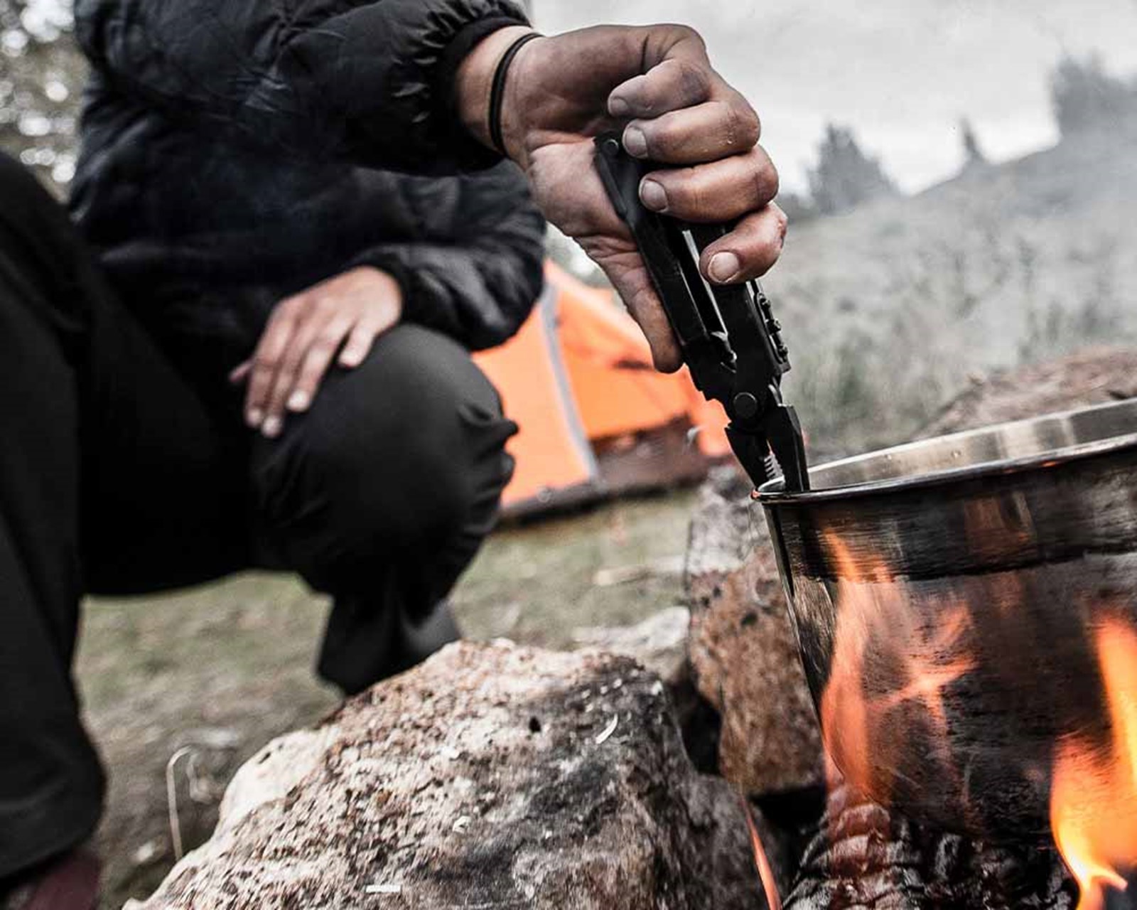 Person der bruger multitool til at justere på en gryde over bål.
