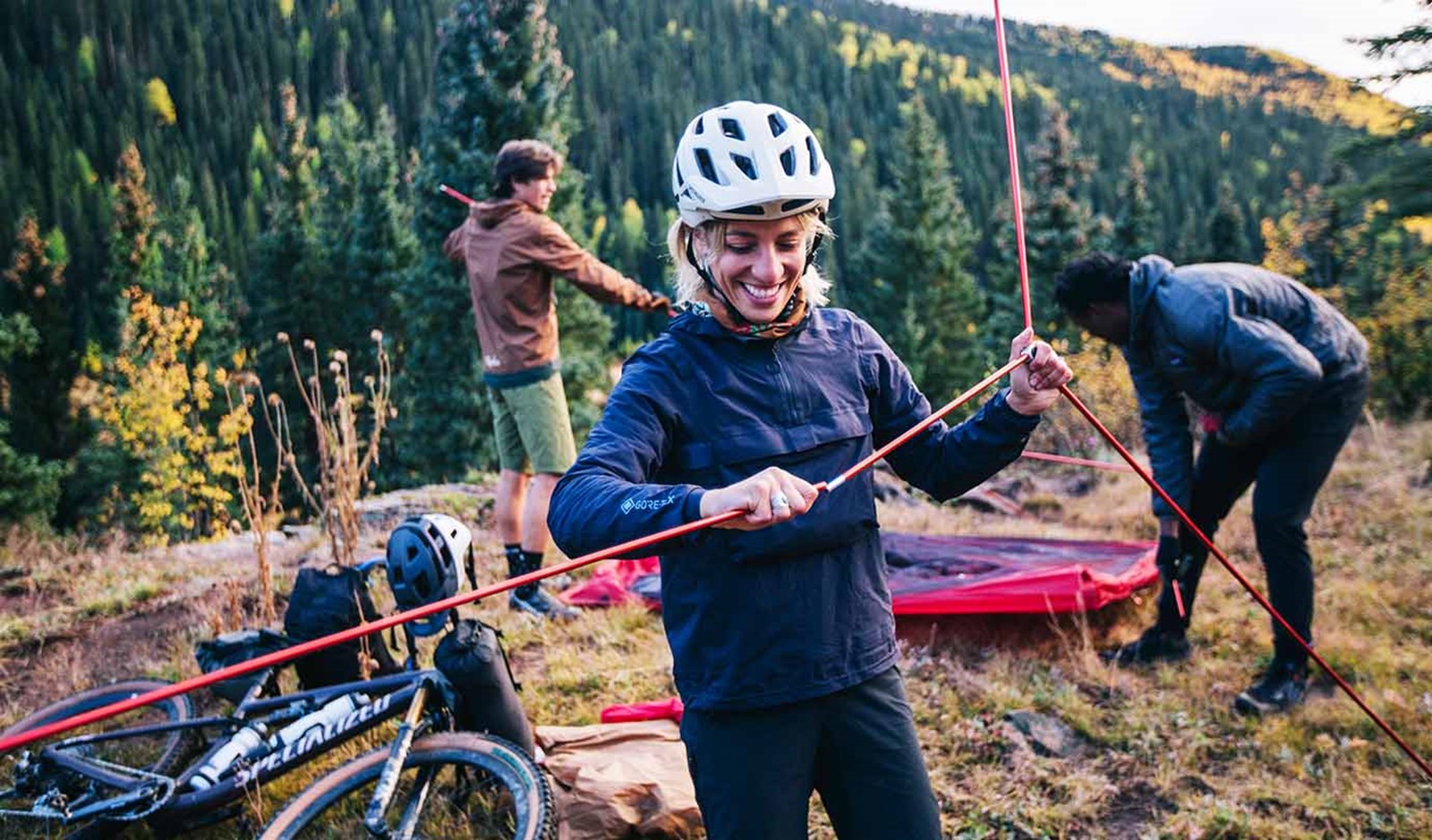 Fol der er ved at sætte telt op, hvor kvinden i forgrunden samler stængerne.