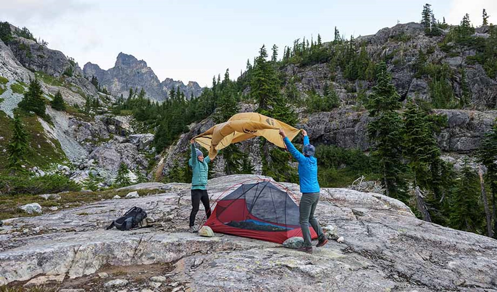 To personer er ved at sætte oversejlet på et telt i bjergene.