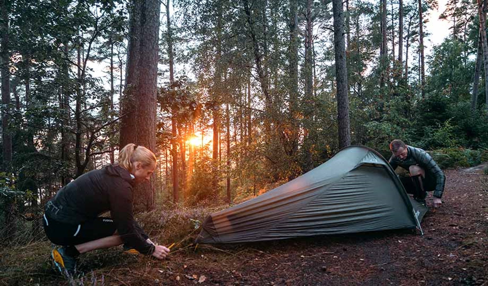 To personer er ved at sætte et telt op og får spændt oversejlet godt ud for at undgå at regnen kommer ind.