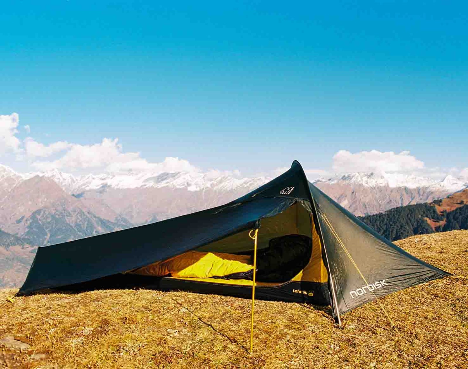 Et nordisk telt slået op på toppen af et bjerg i solskin.