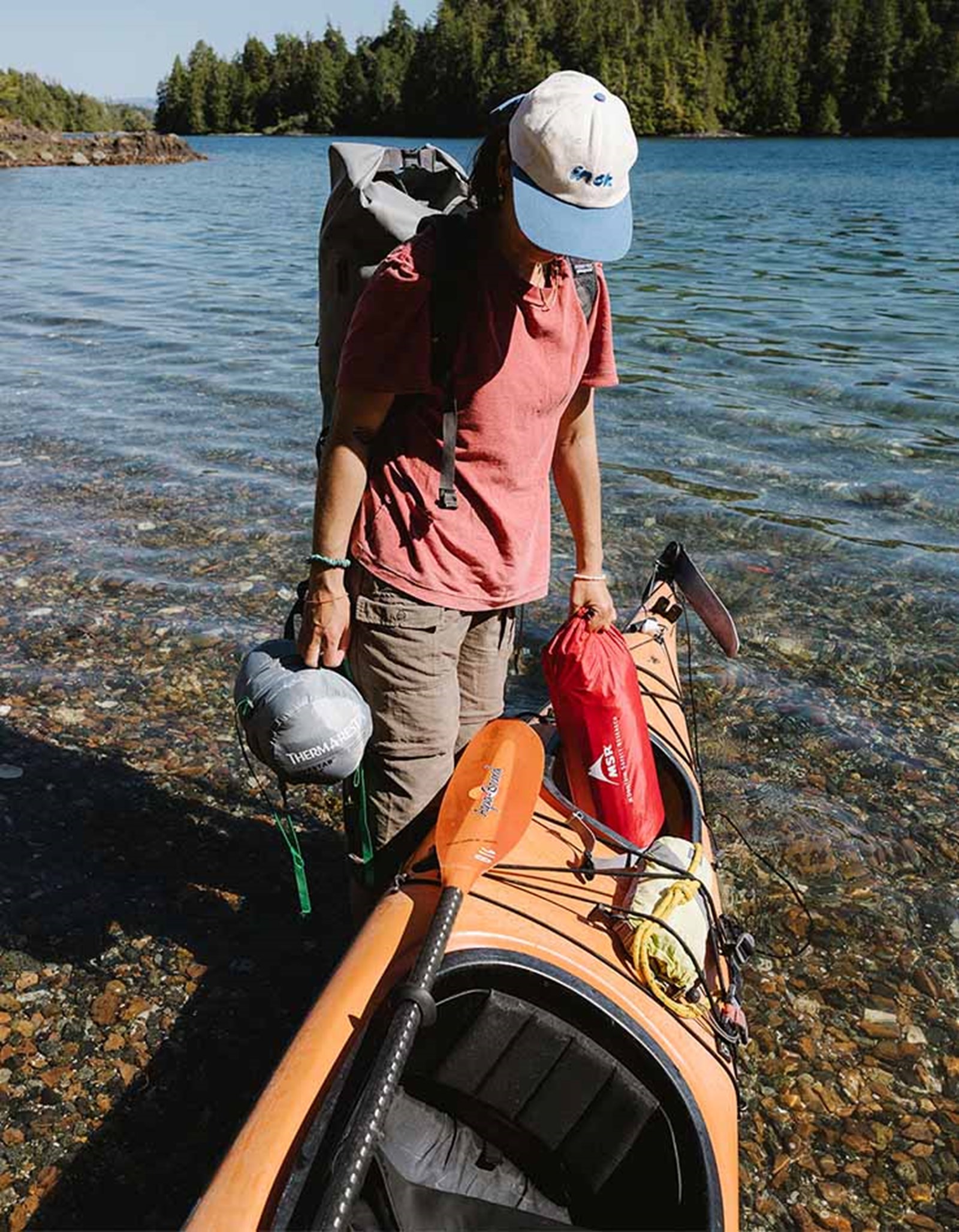 En person er ved at pakke sin kajak med et telt og liggeunderlag.