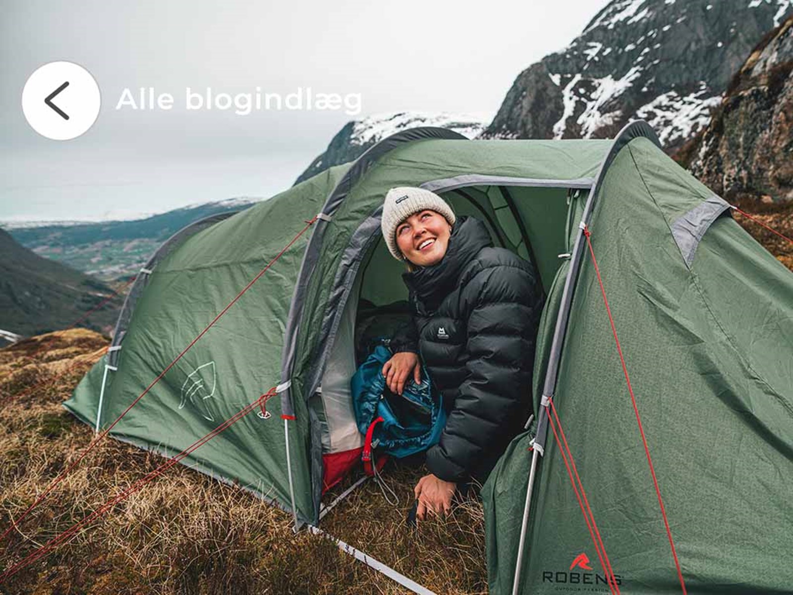 En kvinde der sidder halvt inde i et tunneltelt i bjergene.