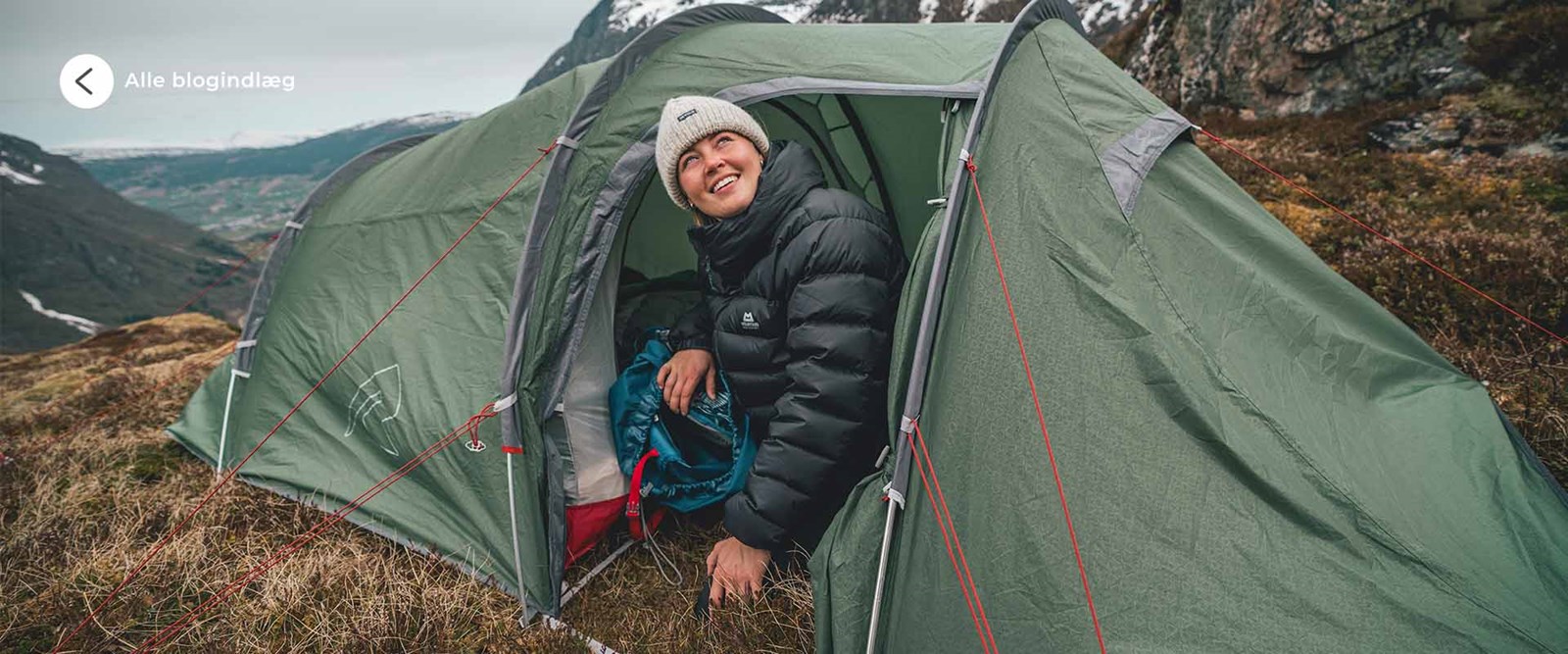 En kvinde der sidder halvt inde i et tunneltelt i bjergene.