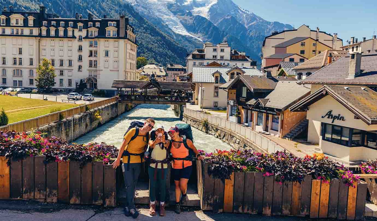 Tre backpackere, der tager et selfie på en bro over en flod.