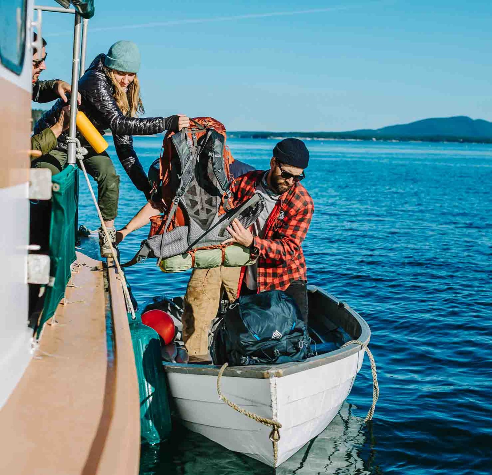 En person løfter en rygsæk over i en robåd.