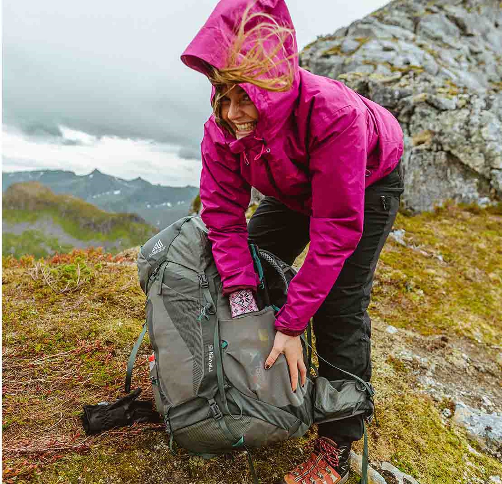 En kvinde står i blæst og prøver at finde noget i sin rygsæk.