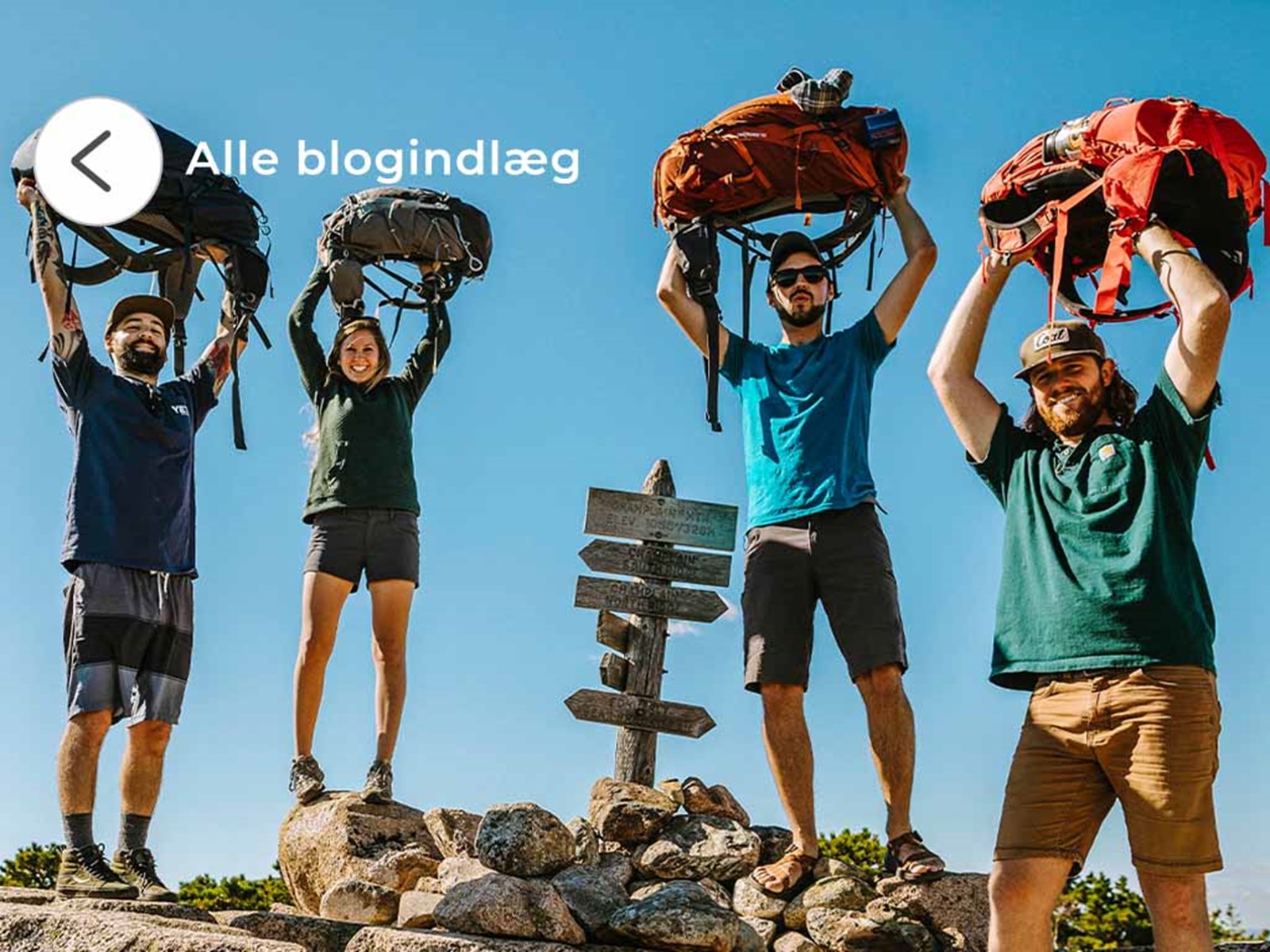 Backpackere der løfter deres rygsæk over hovedet og smiler.