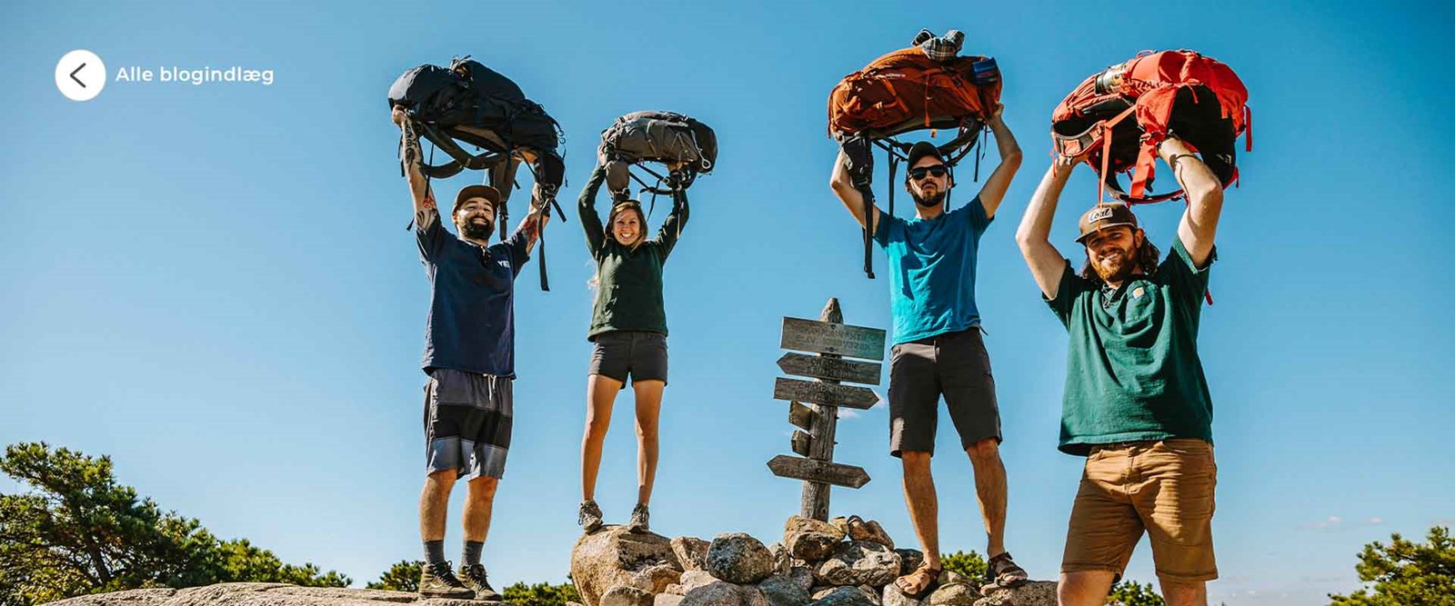 Backpackere der løfter deres rygsæk over hovedet og smiler.