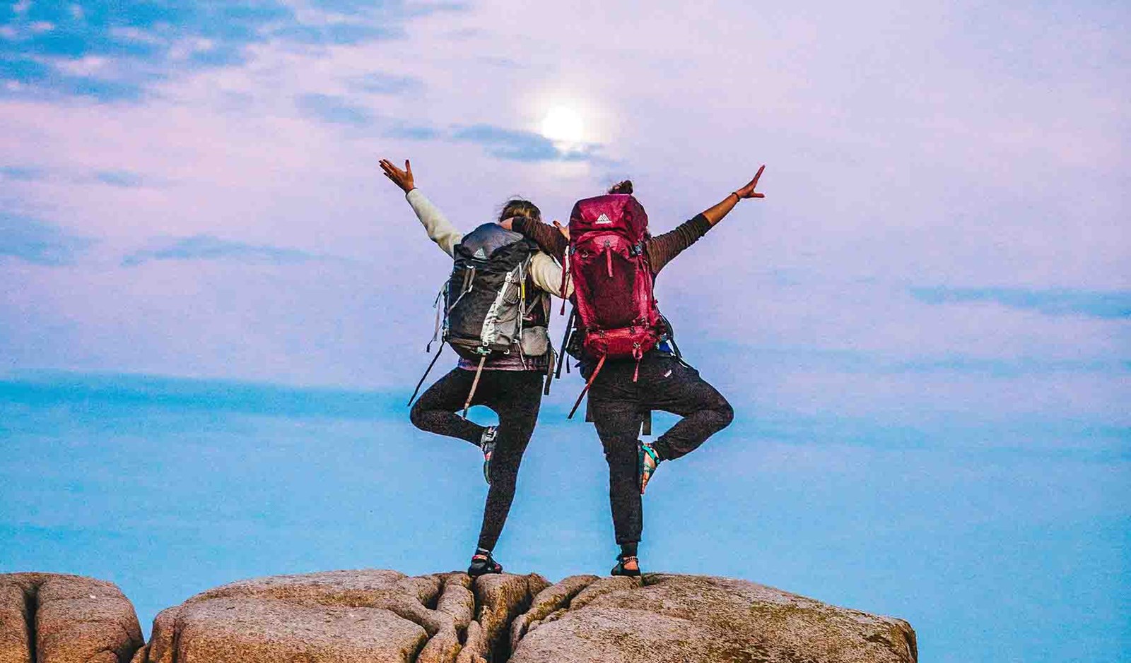 To mennesker der poserer med deres rugsække foran månen.