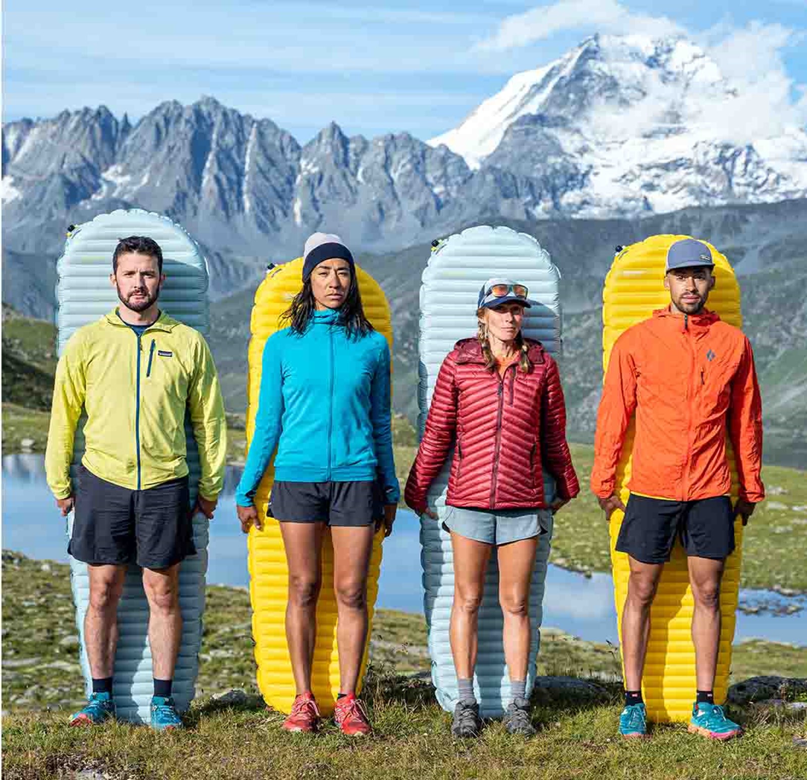 Fire personer på et bjerg med hvert sit liggeunderlag bag ryggen.