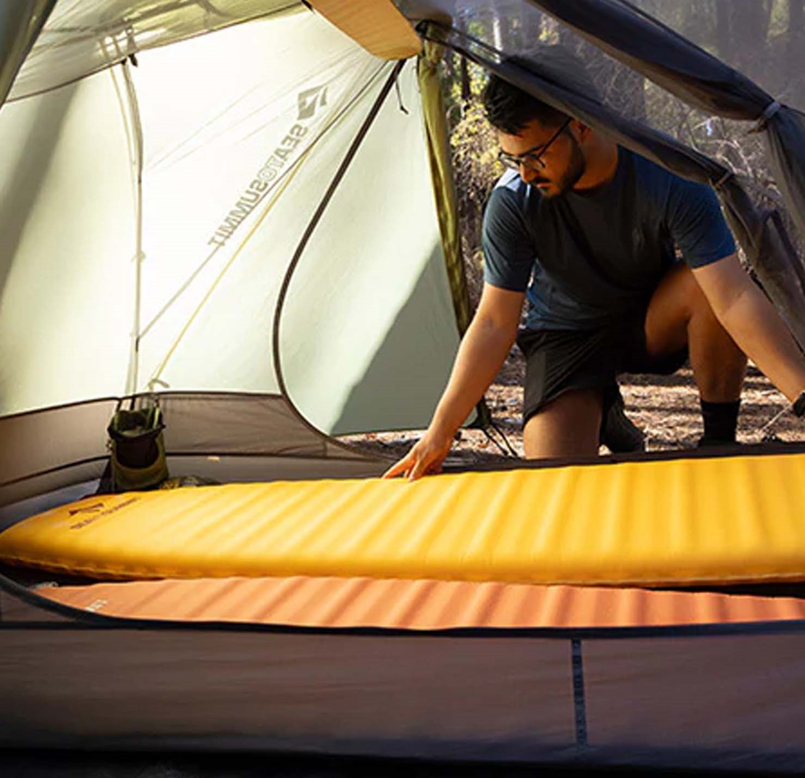 En mand der lægger sit liggeunderlag ind i sit telt.