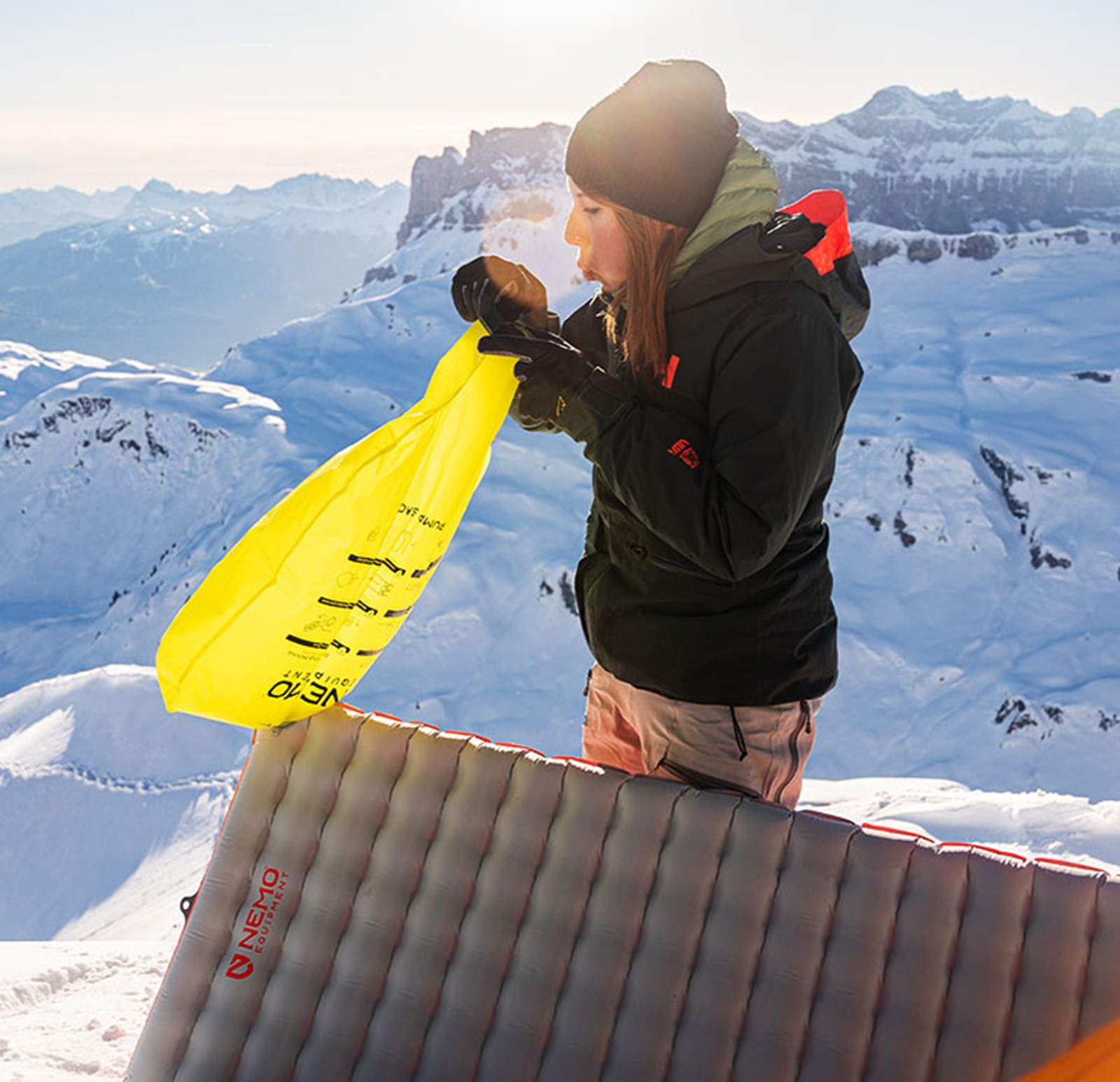 En kvinde puster sit oppustelige liggeunderlag op med en pumpepose i et snelandskab.