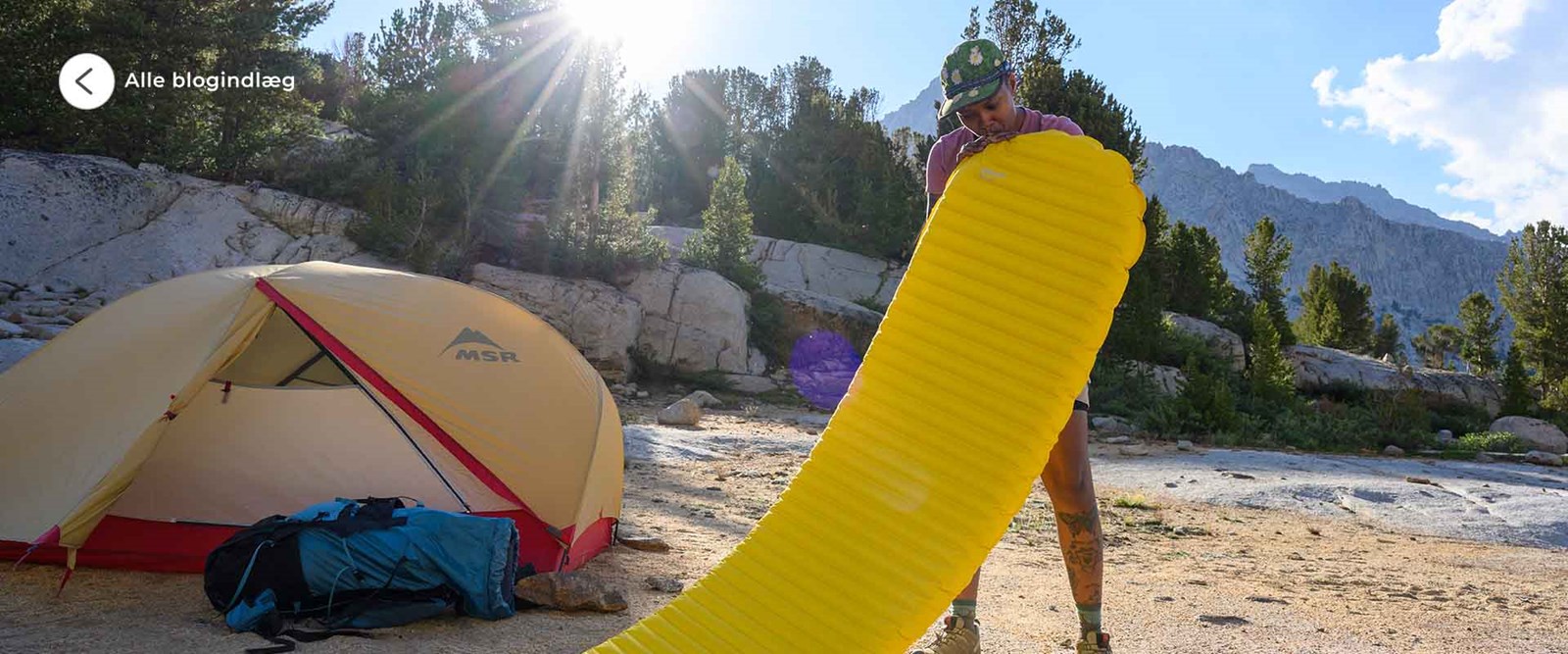 En kvinde der er ved at puste sit liggeunderlag op foran hendes telt.