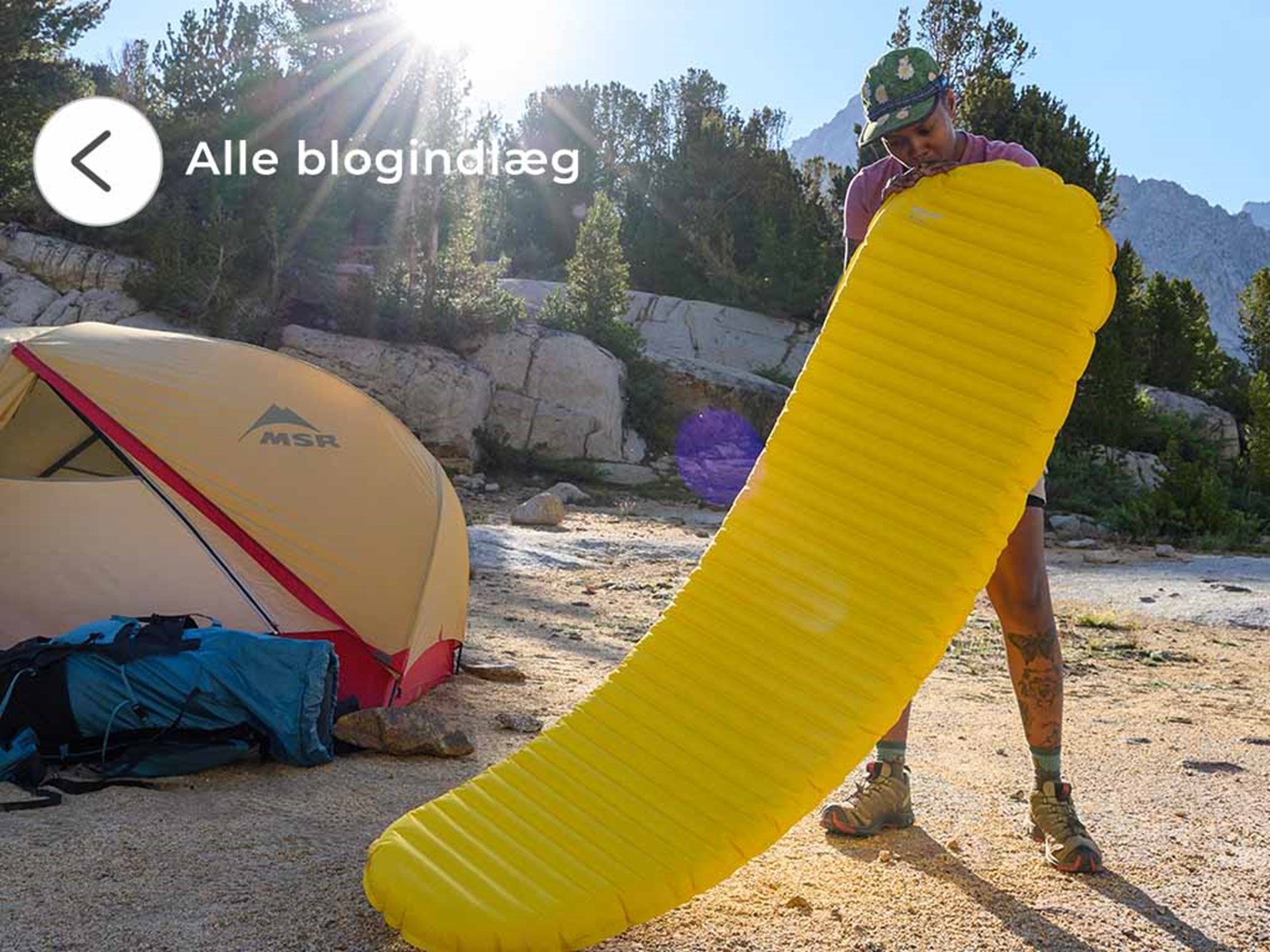 En kvinde der er ved at puste sit liggeunderlag op foran hendes telt.