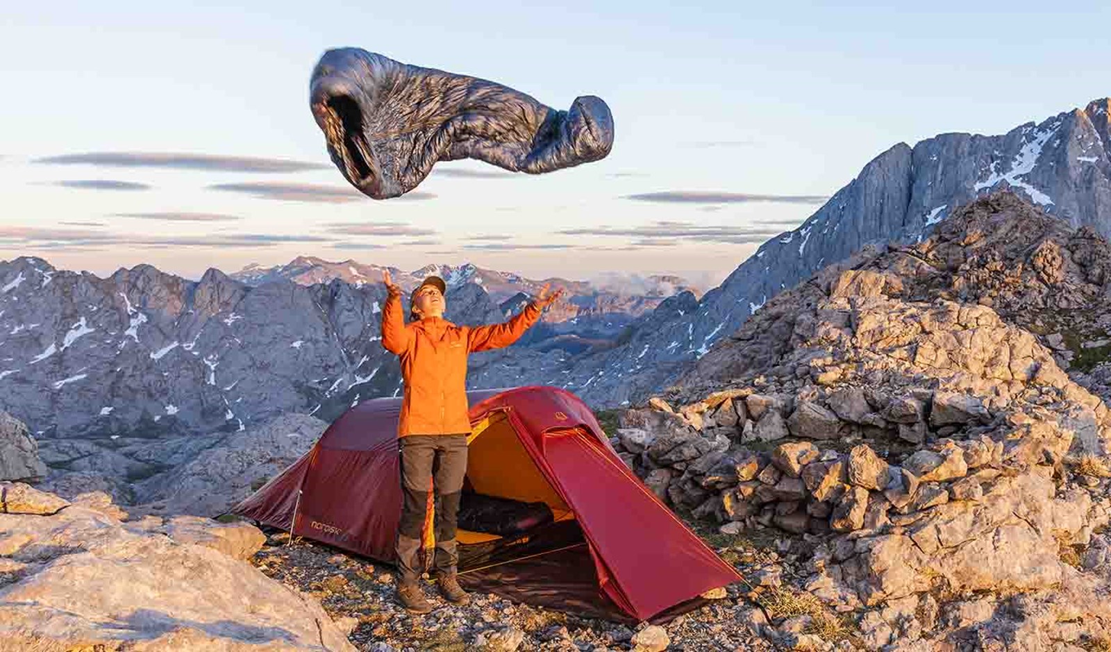 En kvinde kaster sin dunsovepose op i luften foran sit telt.