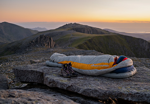 Mand i sovepose på toppen af en klippe med smuk solnedgang