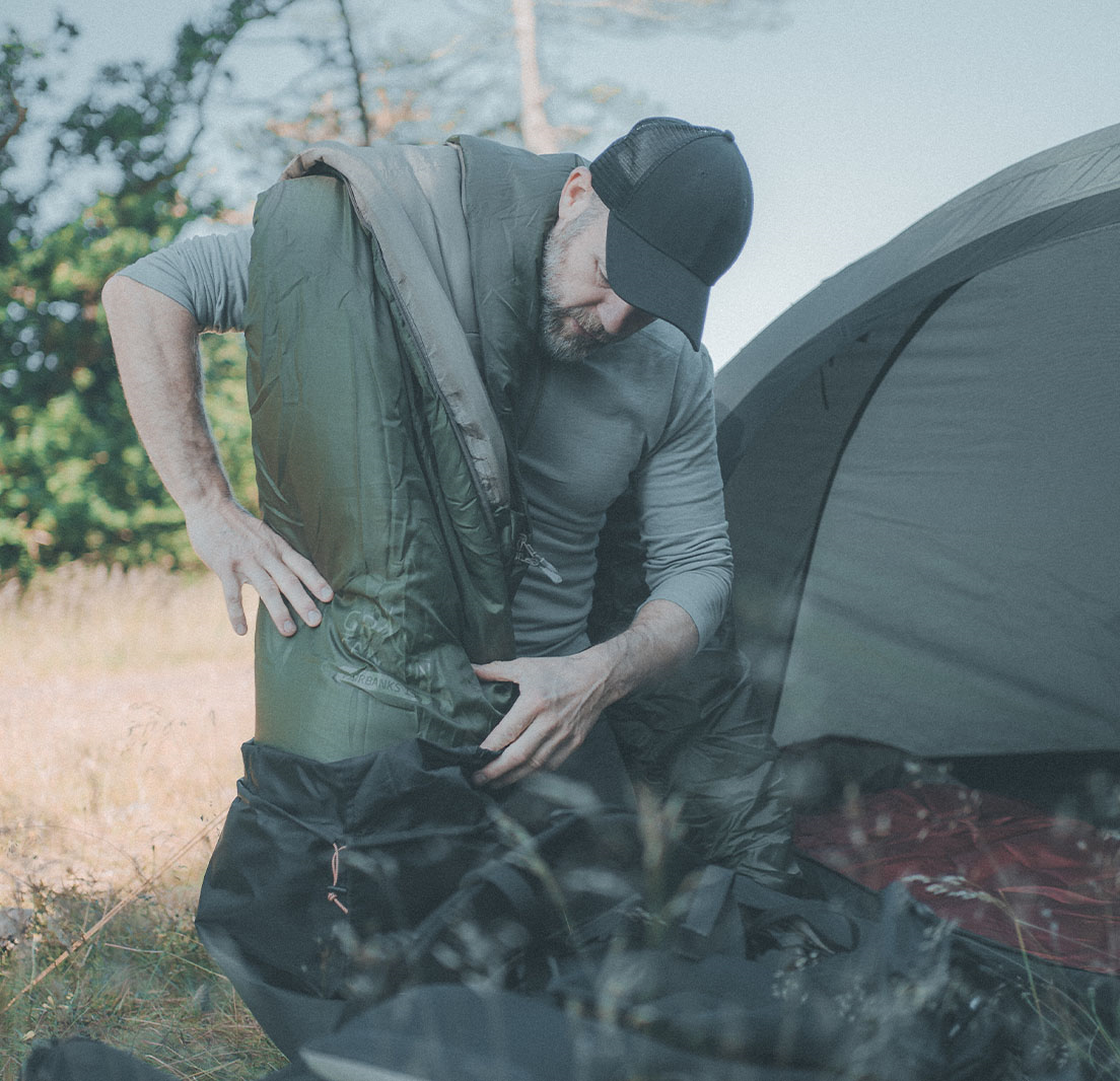 Mand forsøger at pakke sin sovepose sammen