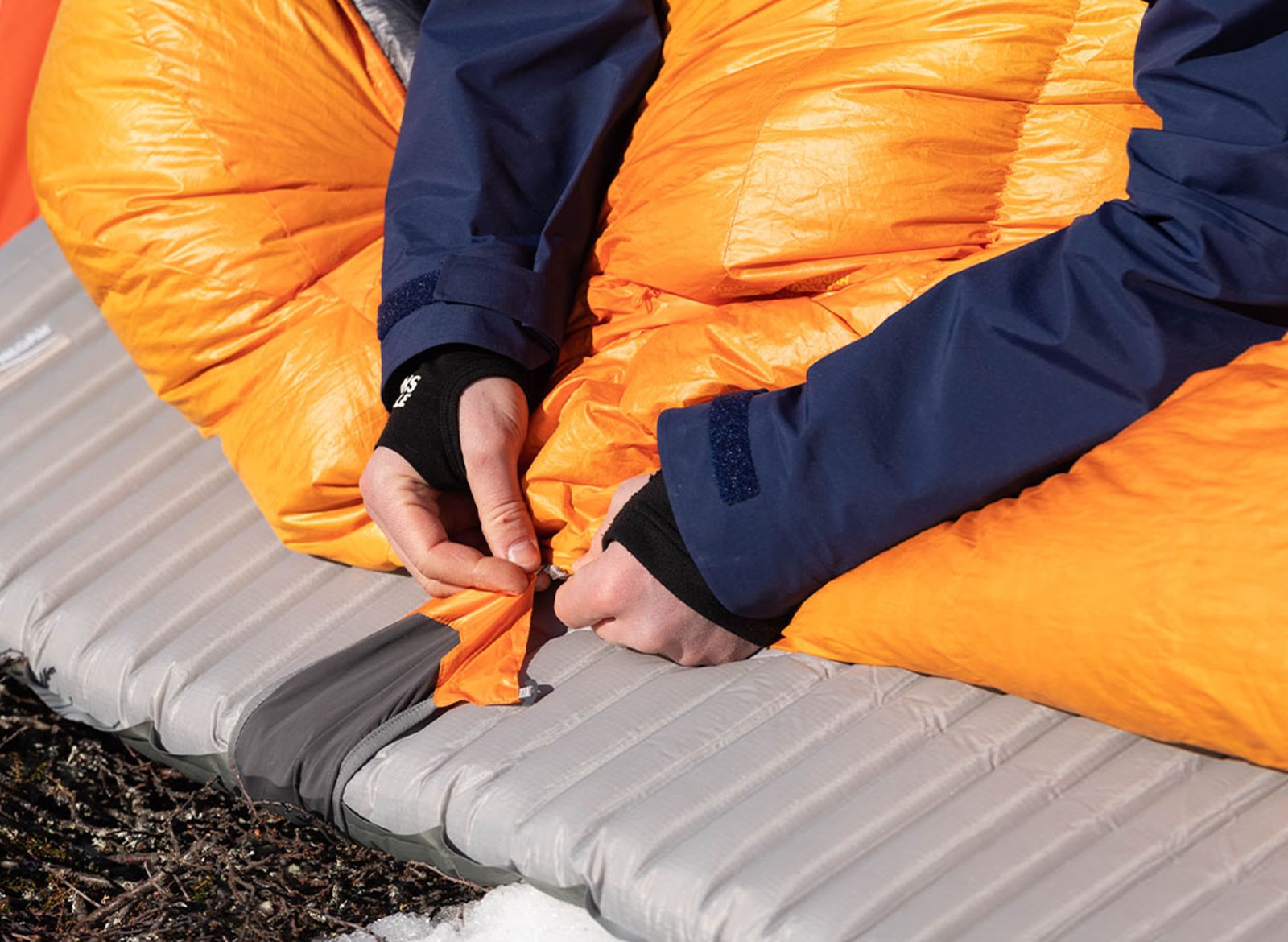 En person der fæstner sin sovepose til liggeunderlaget.