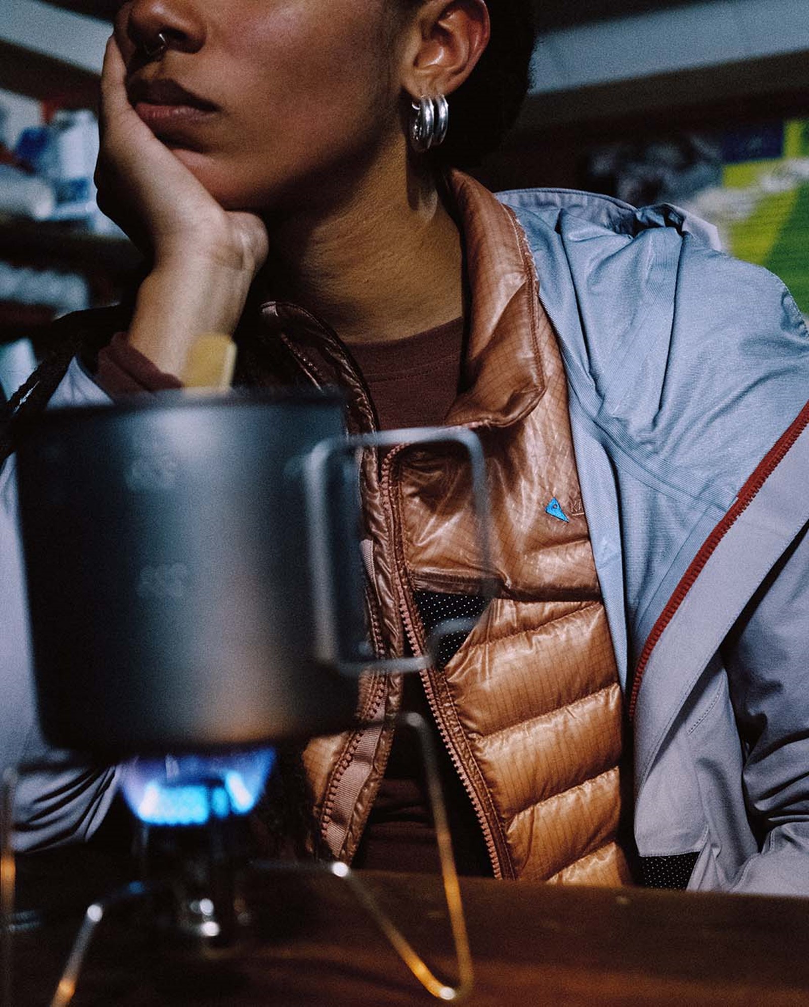 En kvinde der laver mad iført en dunjakke med en skaljakke over.