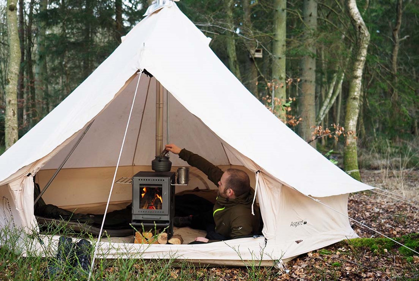Mand der varmer vand på en teltovn i et bomuldstelt