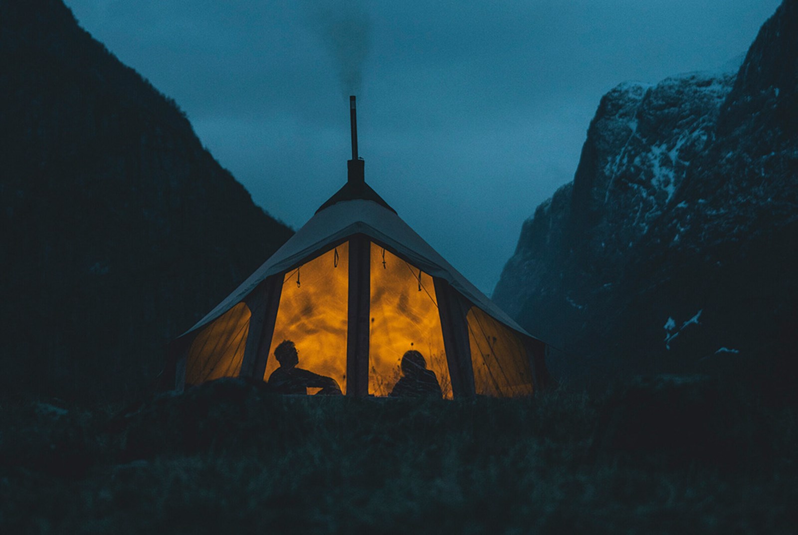 Folk der sidder i en opvarmet lavvu om aftenen.