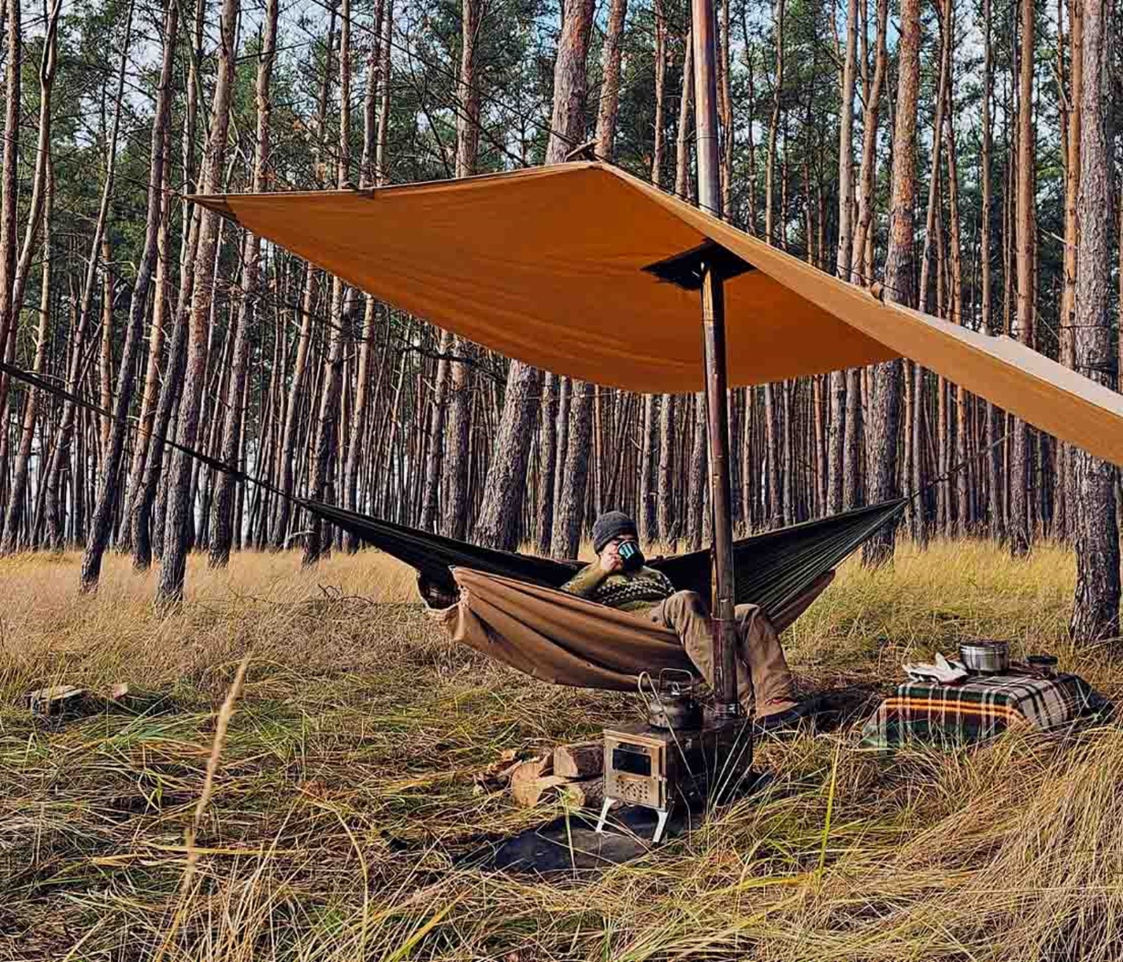 Mand der ligger i en hængekøje under en Hot Tarp med teltovnen kørende.