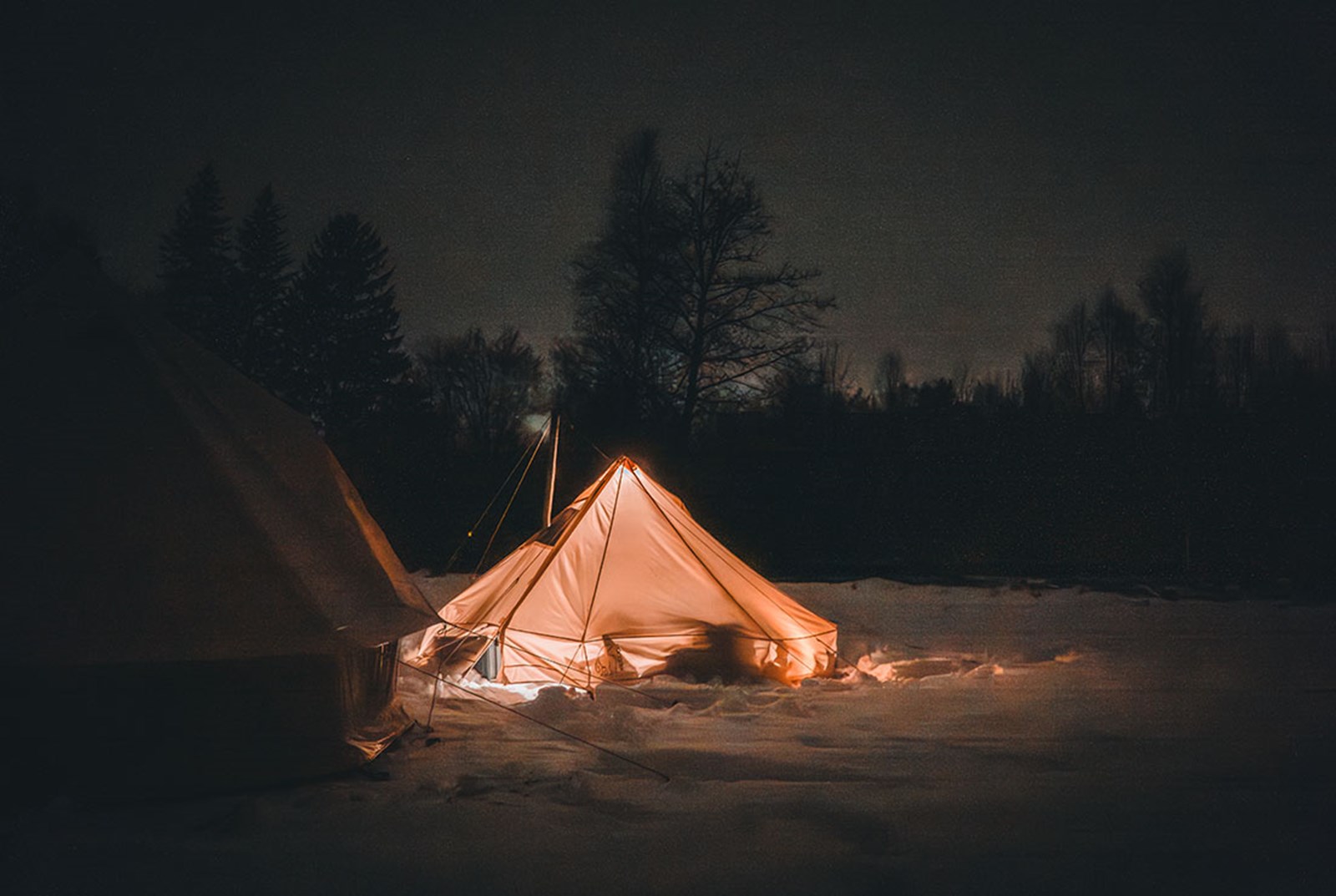 Et bomuldstelt der lyser op i mørket, fordi teltovnen er tændt.