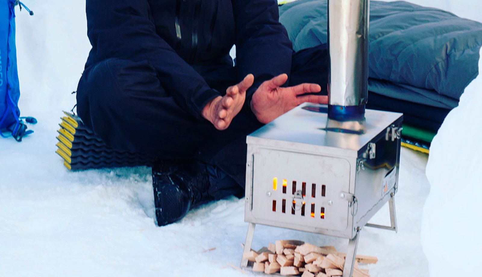 En person varmer hænderne på en teltovn.