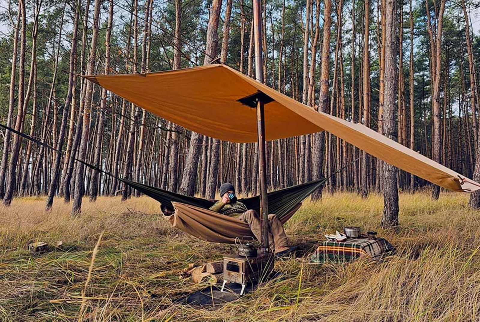 Mand der sidder i en hængekøje under en tarp med en teltovn.