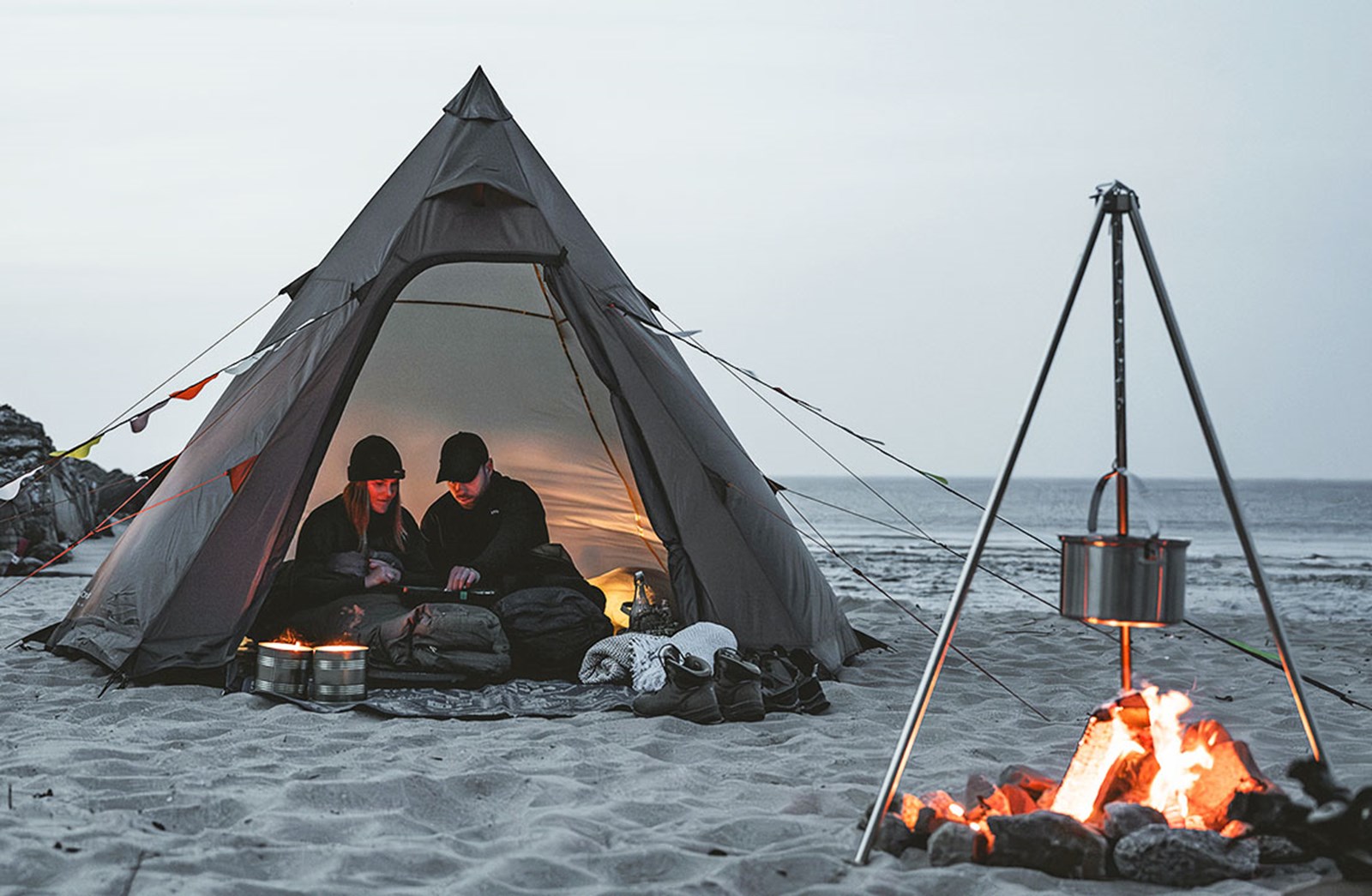 Et par i en tipi fra Easy Camp med et bål på stranden.