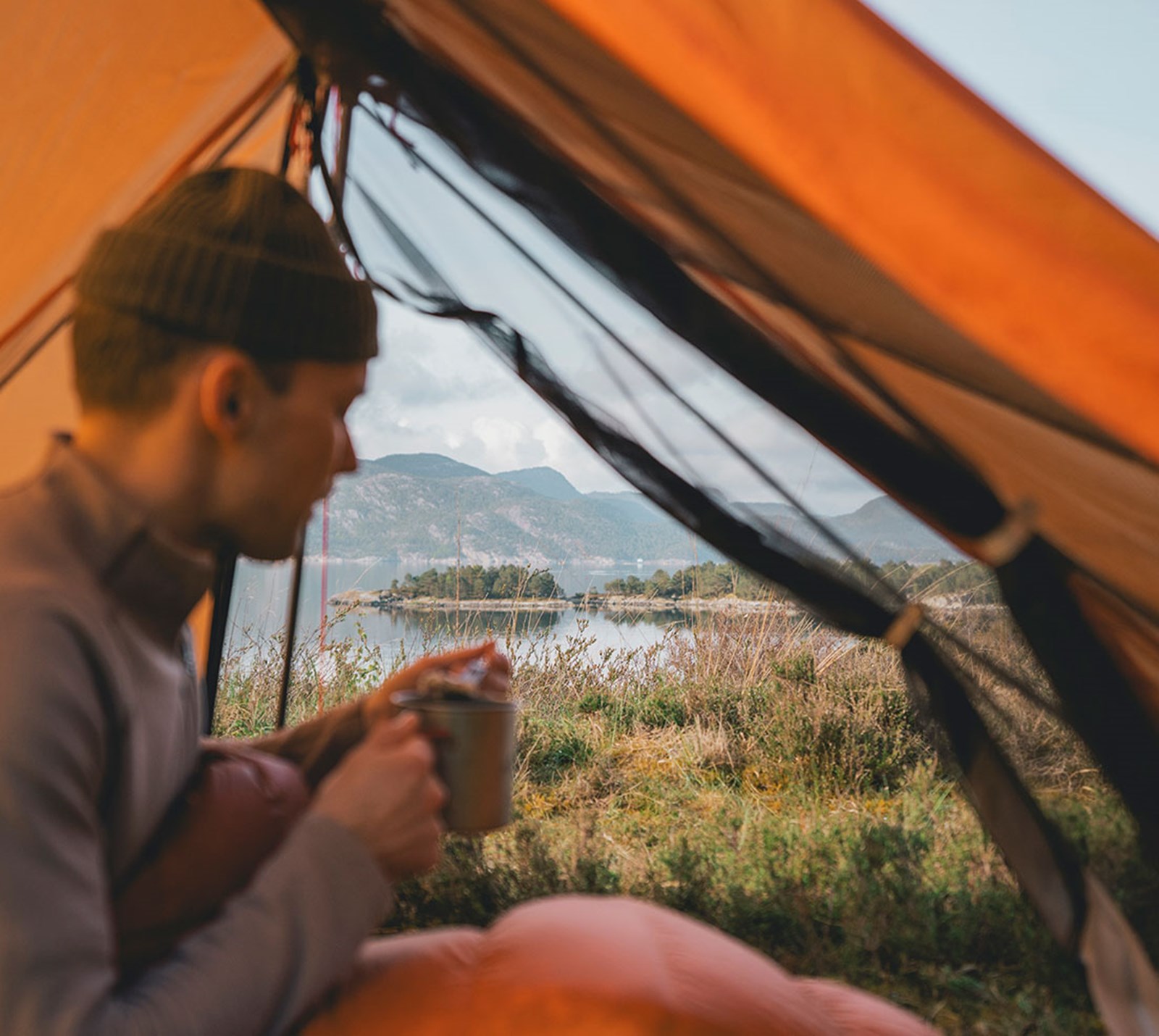 Person der sidder i teltet med en varm kop med åbent i begge sider.