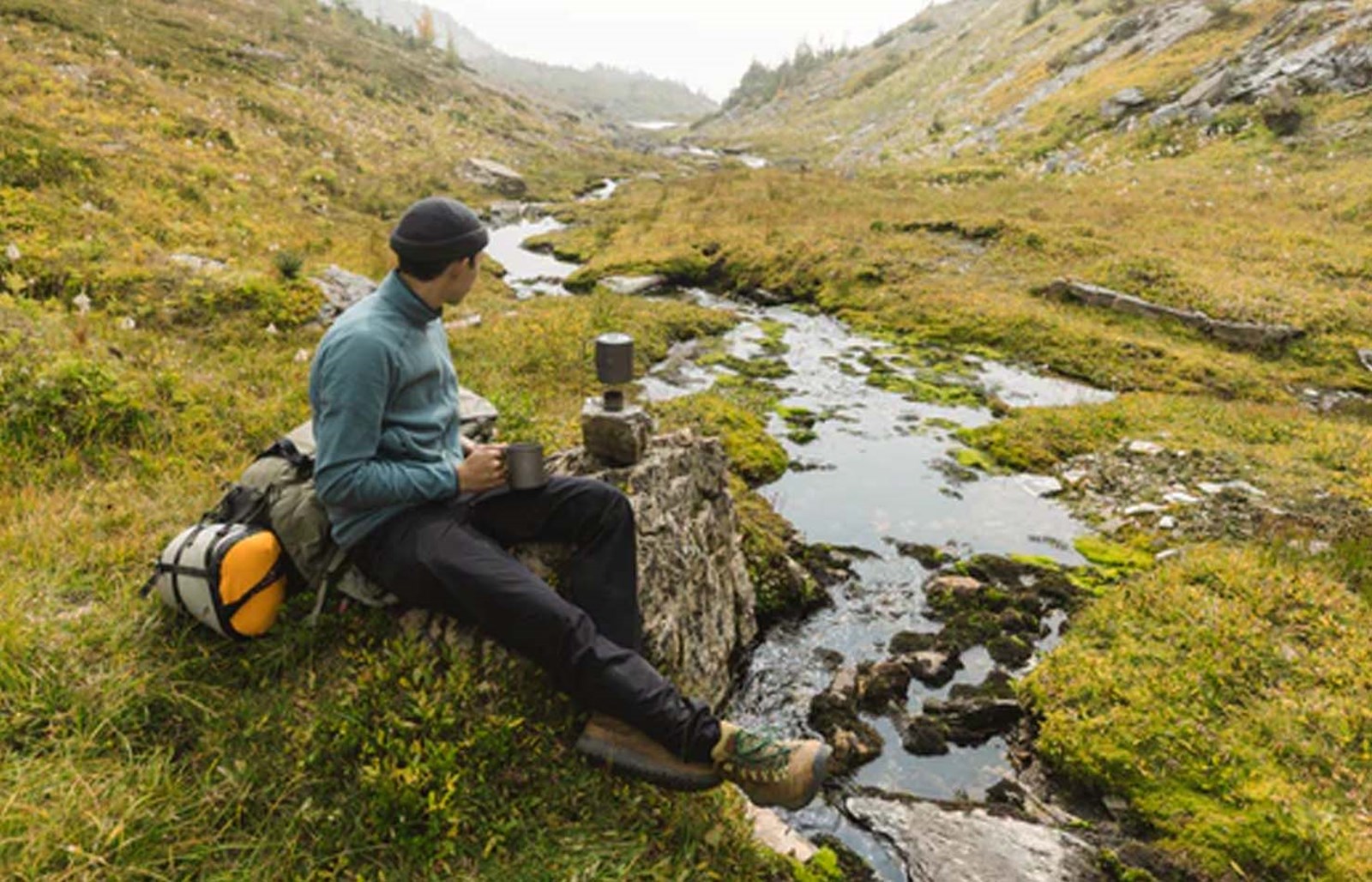 Mand der laver mad med sit toaks kogesæt ved et vandløb.
