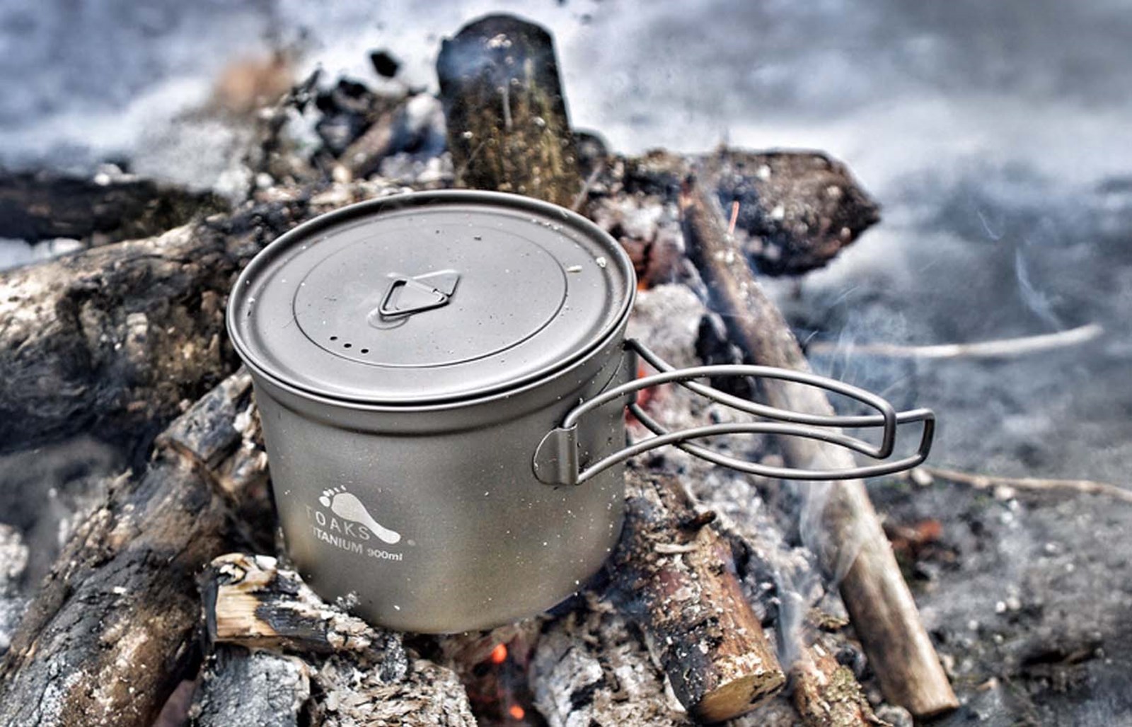 En toaksgryde der står oveni gløderne på et bål.