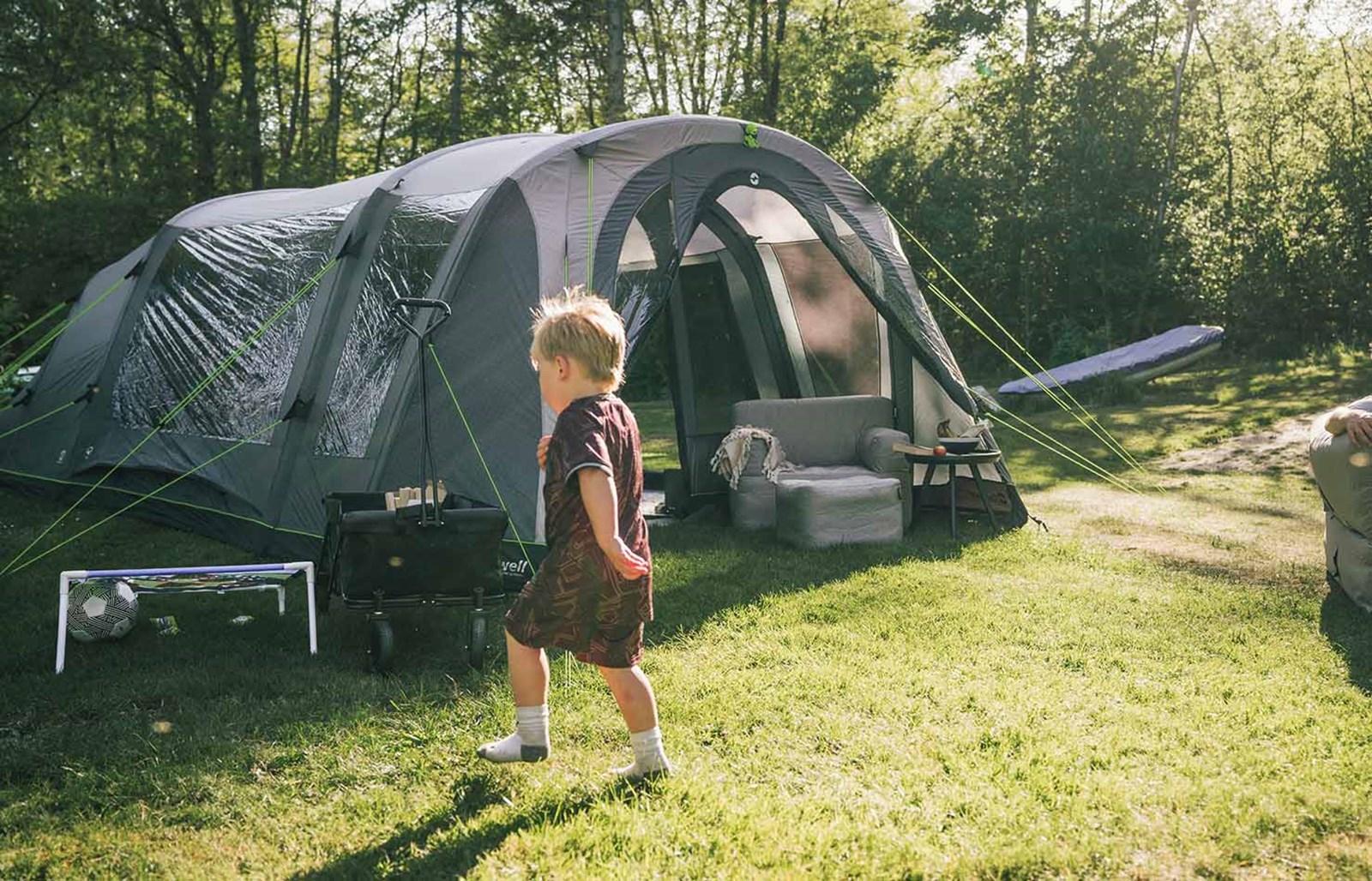 Et barn der spiller bold på græsset foran deres oppustelige Outwell-teltet.