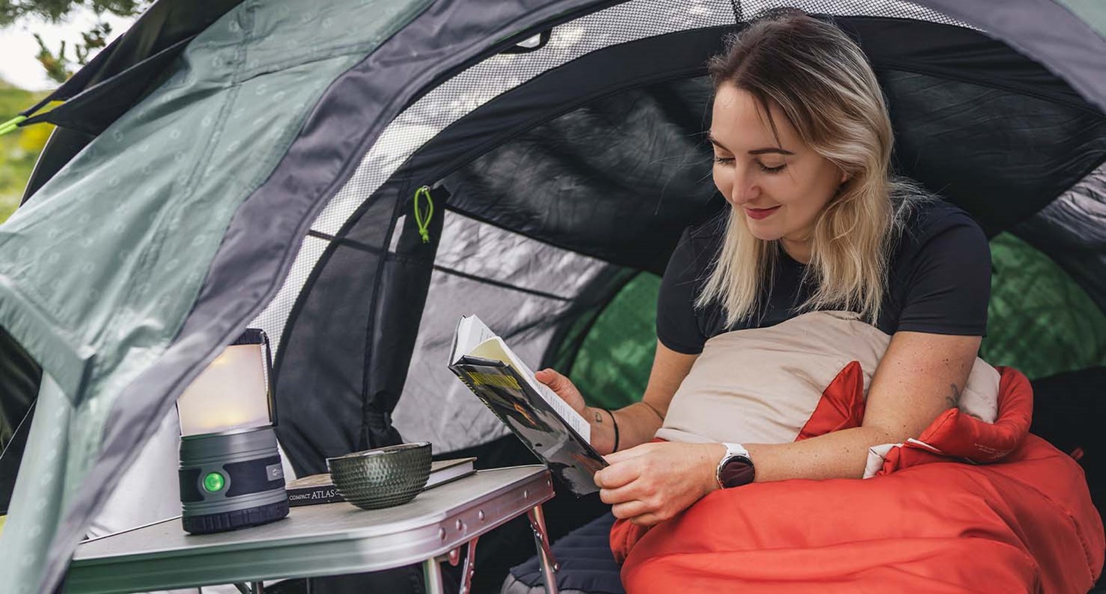 En kvinde der læser i sin bog, i en sovepose i et Outwell-telt.