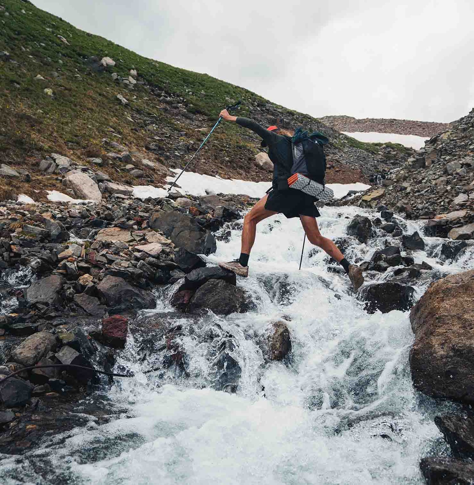 Person der krydser et vandfald med sine vandrestave.