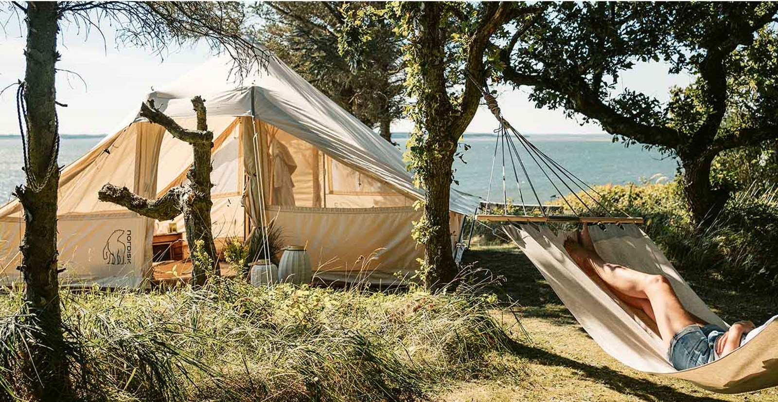 Bomuldstelt i det fri og en person i en hængekøje.